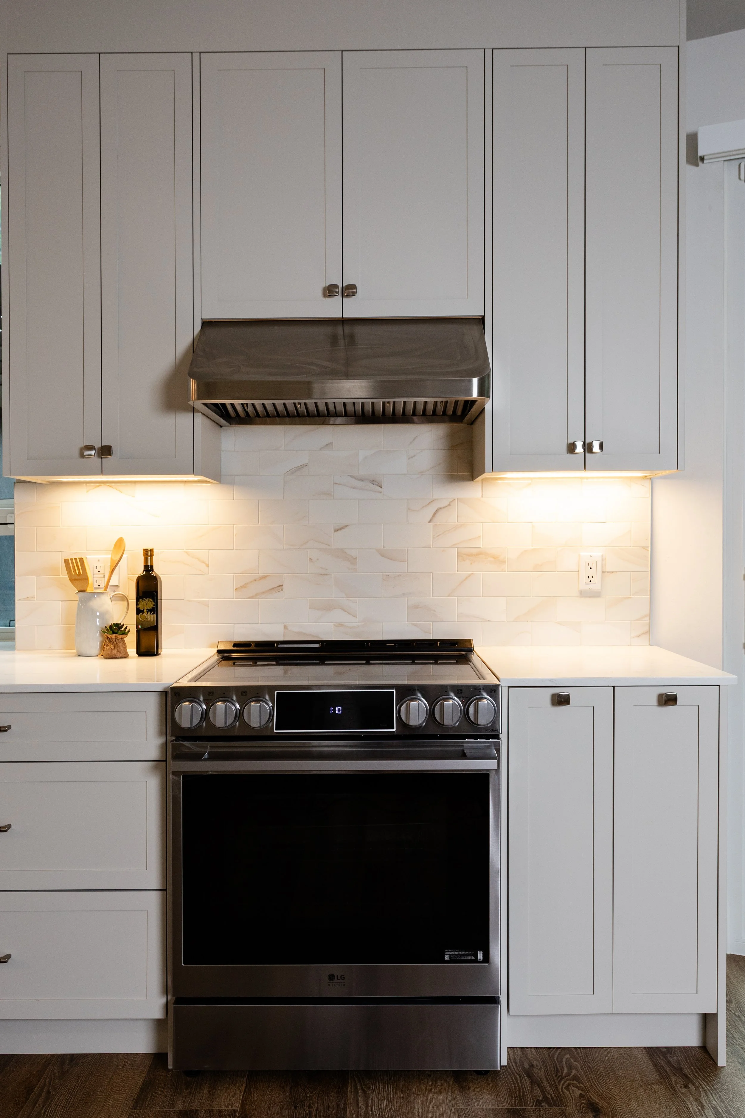 Modern kitchen with white cabinets, stainless steel oven and stove, marble backsplash, and decorative items on the counter.
