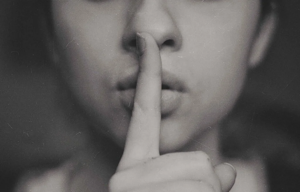 a woman has a finger over her lips signifying the rule of don't speak