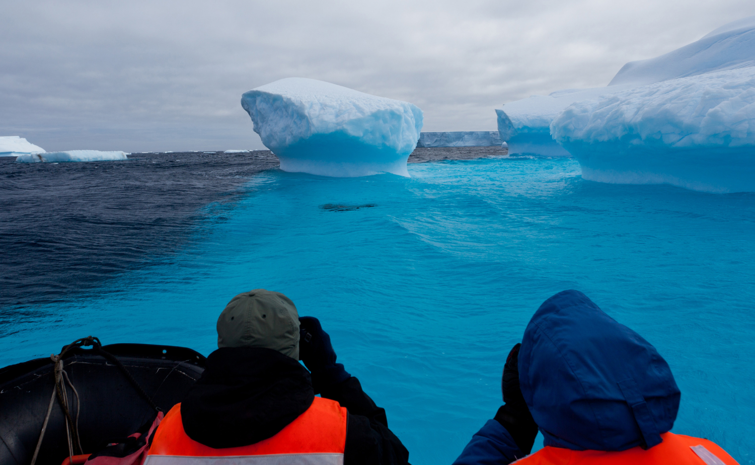 Expedition travelers in a Zodiac boat cruising among enormous icebergs in Antarctica