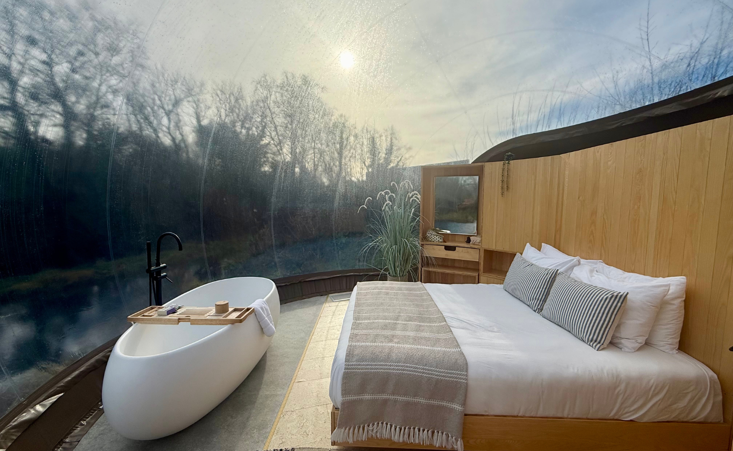 Interior of a Premium River Bubble at Finn Lough with a bed, freestanding bathtub, wood accents, and panoramic views through the transparent dome.