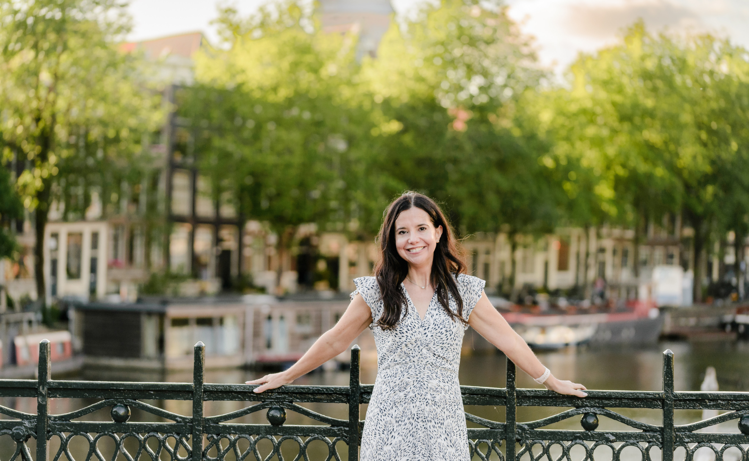 A woman standing on a bridge in Amsterdam at golden hour, showcasing European city charm and canalside travel.