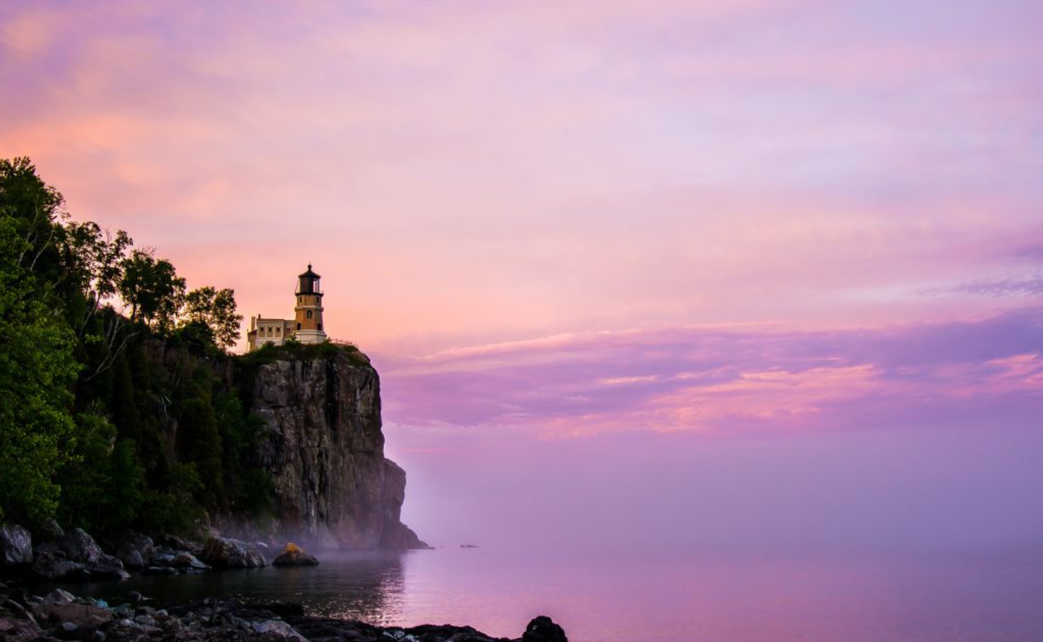 Split Rock Lighthouse stands atop a rocky cliff at sunset, overlooking Lake Superior.