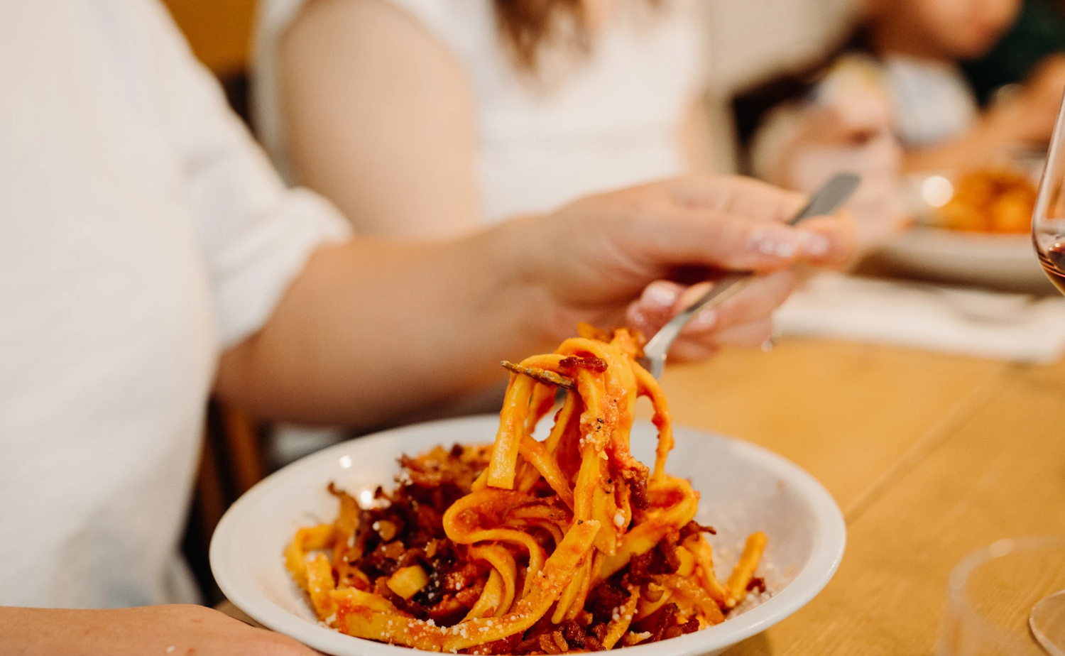 A close-up of fresh pasta in a rich tomato sauce being lifted with a fork during a meal at a restaurant in Rome.