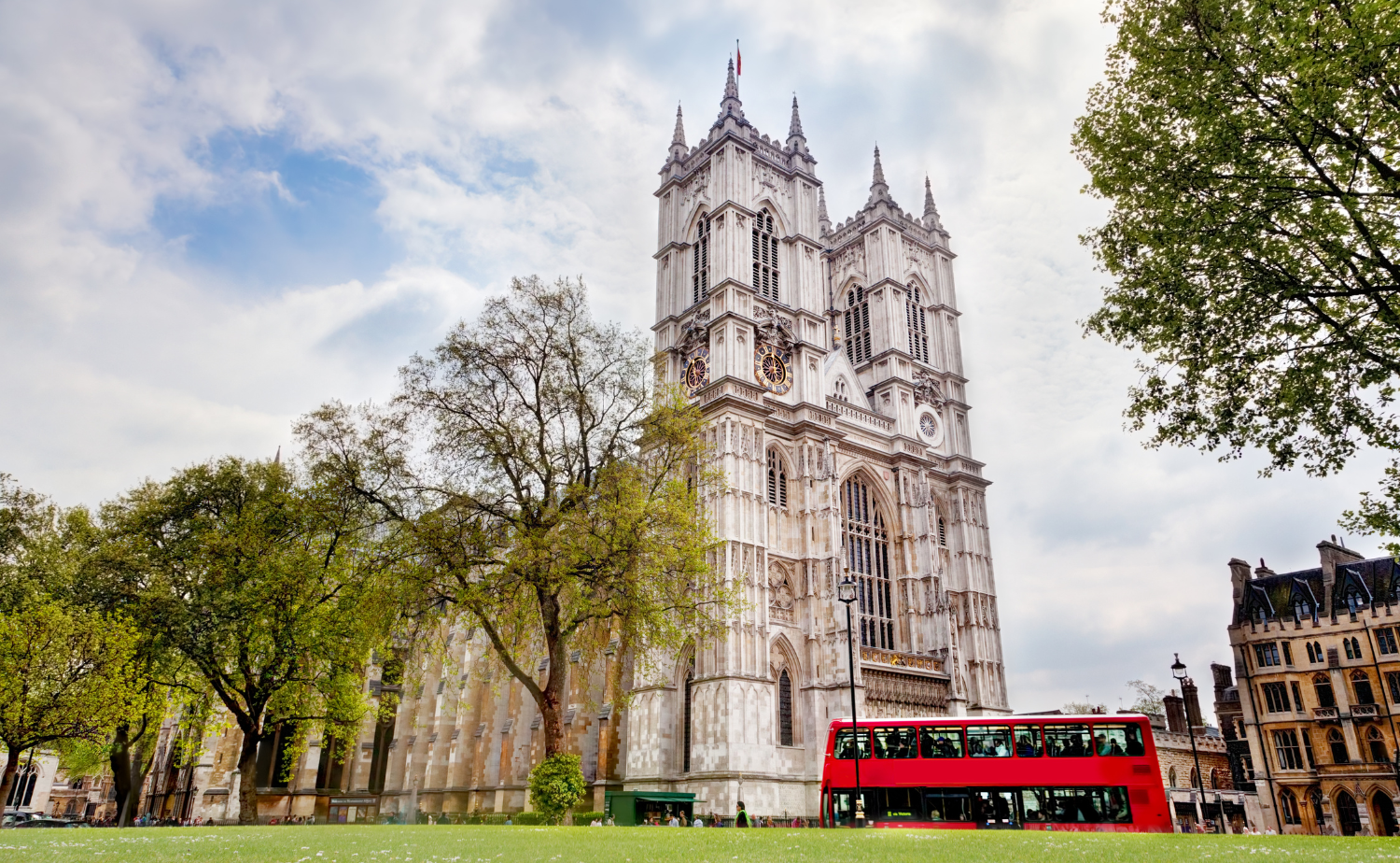 Exterior view of Westminster Abbey in London with a red double-decker bus passing in the foreground.