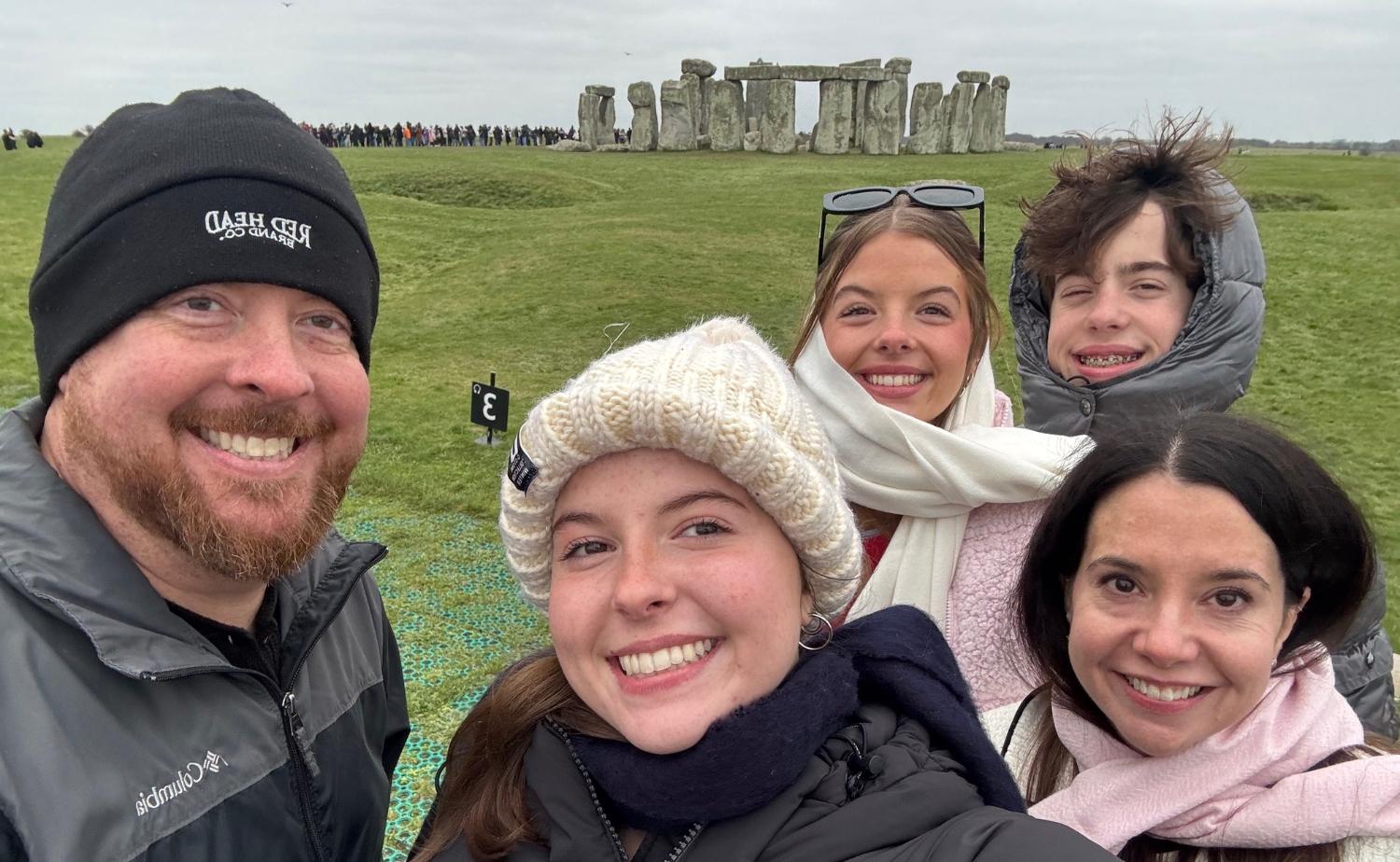 Family standing in front of Stonehenge on a cloudy day during a day trip from London.