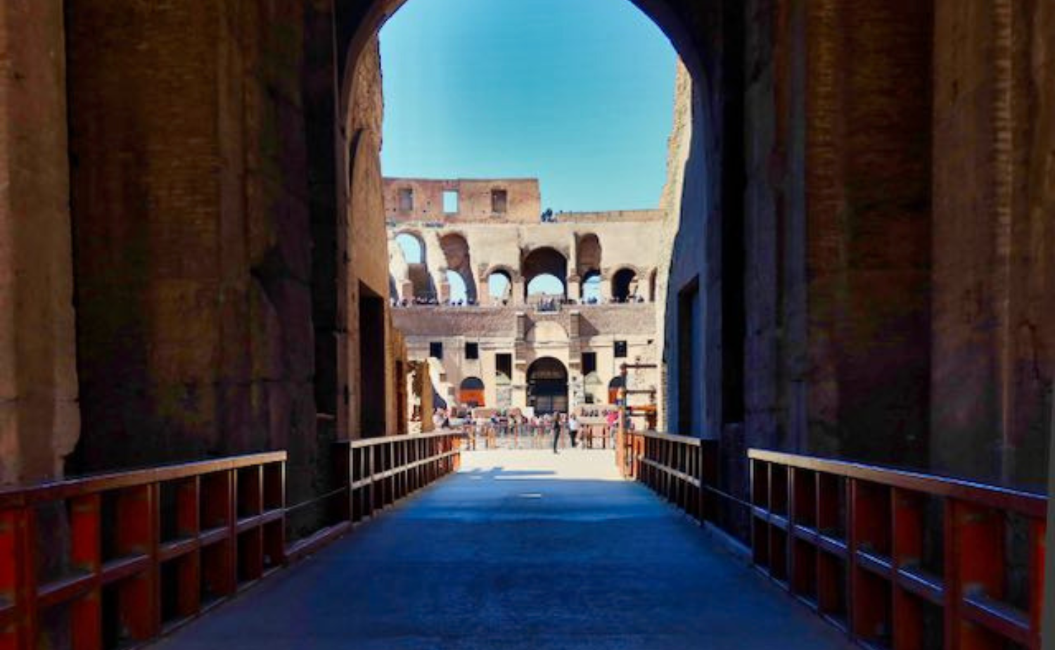A view of the Colosseum framed by a stone archway, with visitors walking across a sunlit path inside the ancient structure.