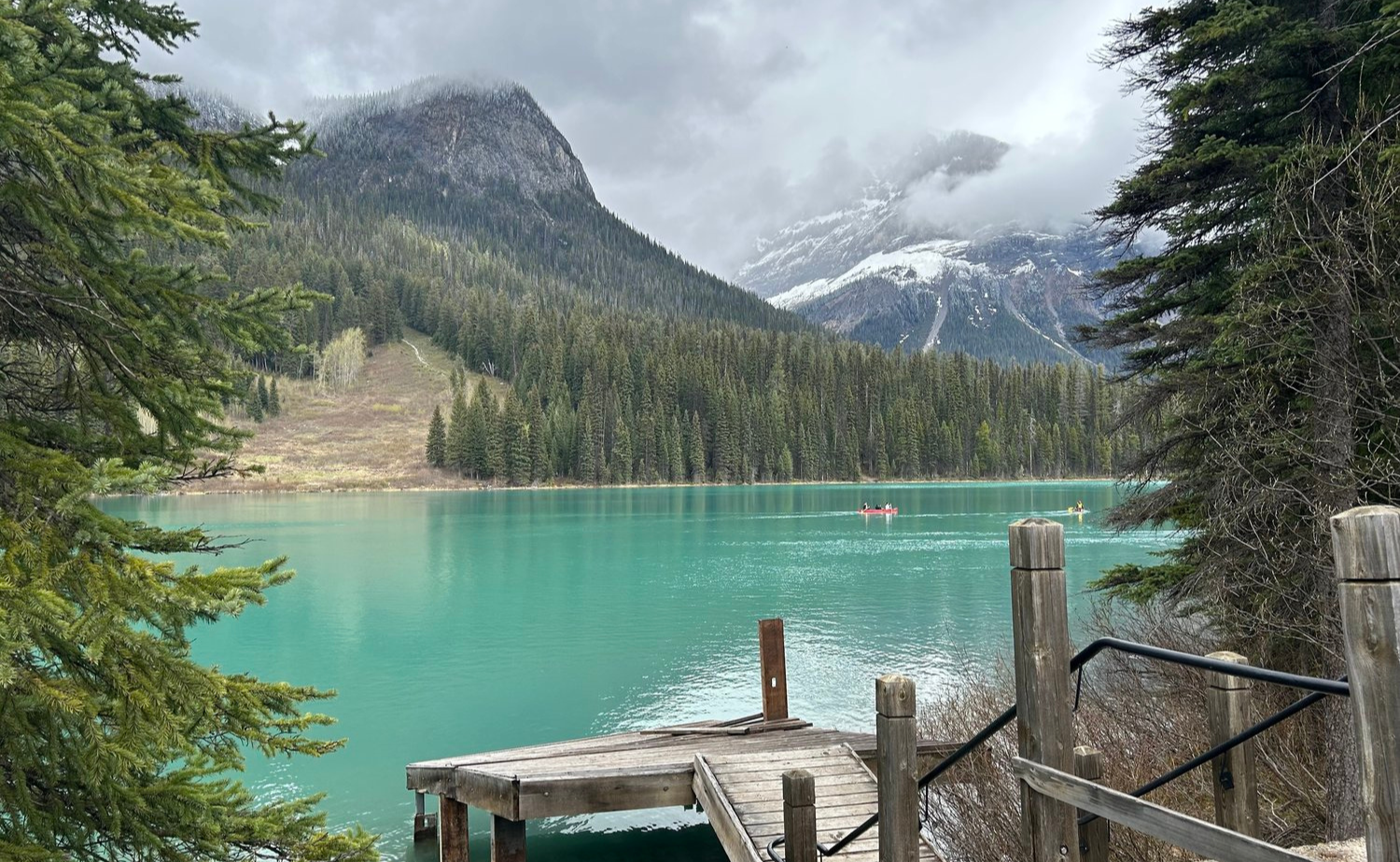 Scenic view of Emerald Lake with a small wooden dock, turquoise water, canoes, and snow-dusted mountain peaks.