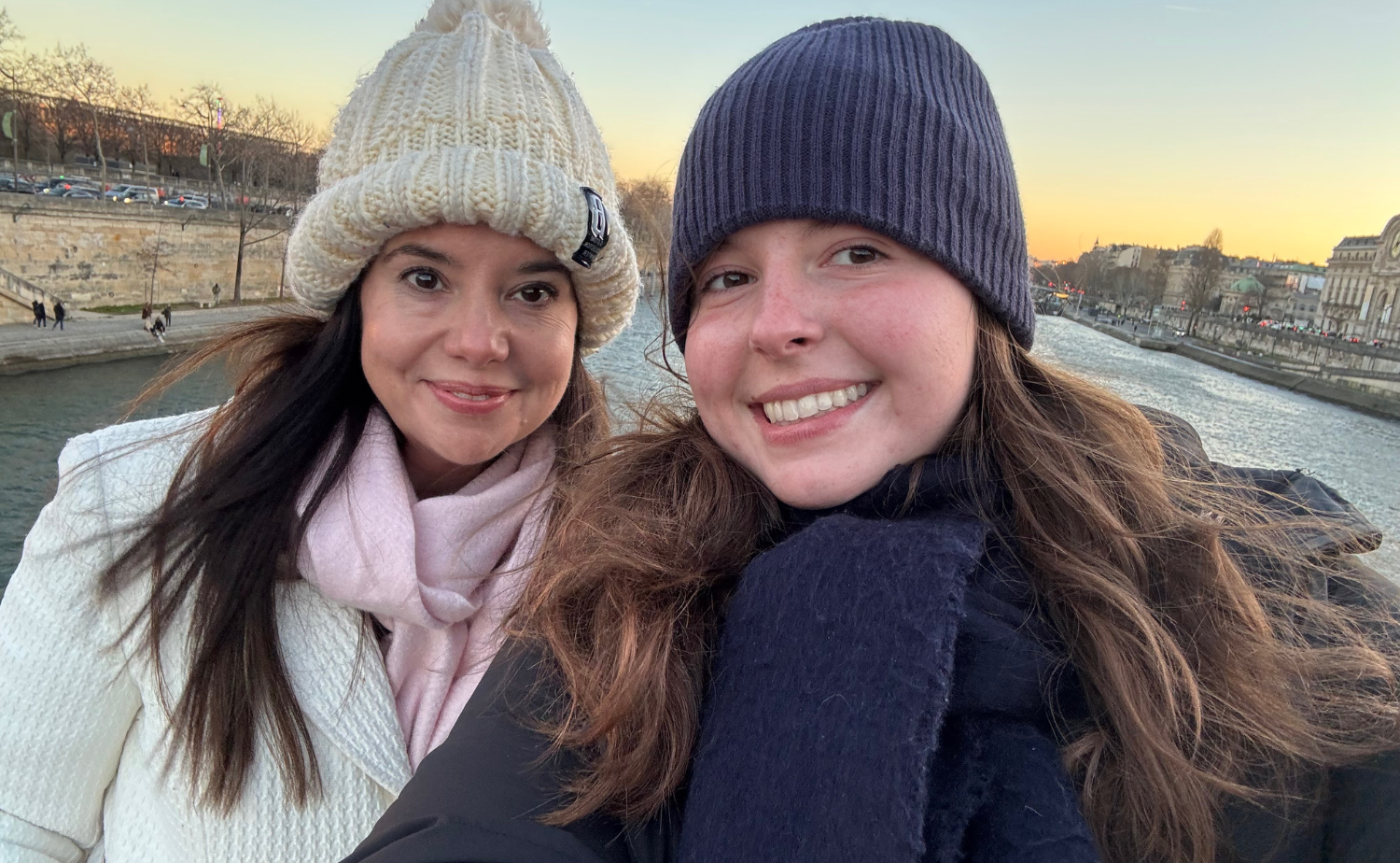 Mother and daughter taking a selfie along the Seine River at sunset in Paris.