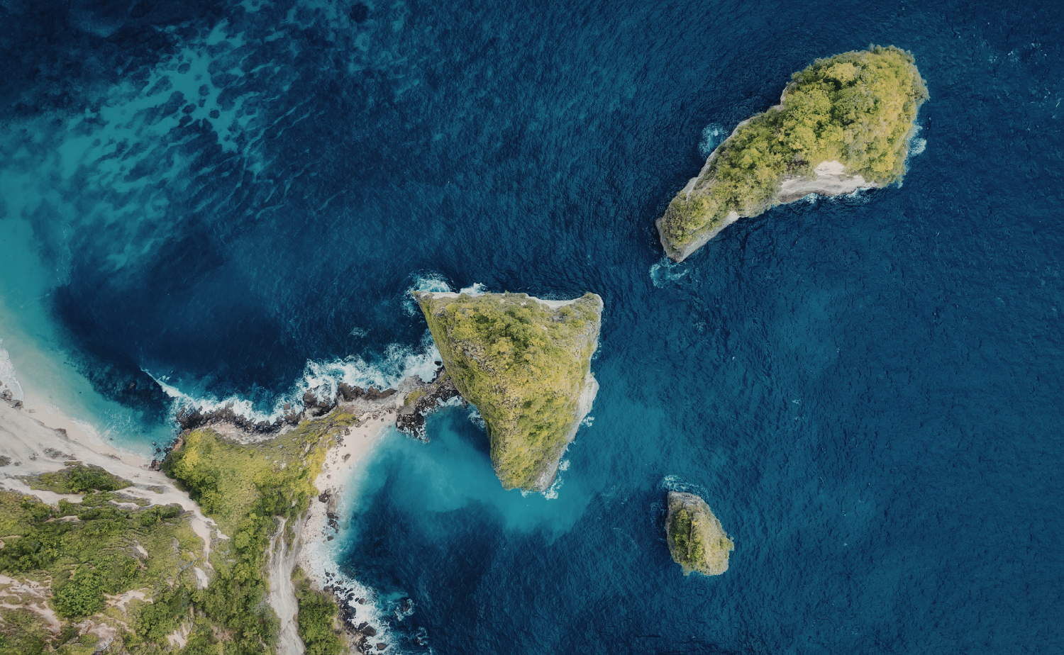 Aerial view of lush green island cliffs surrounded by deep blue Pacific Ocean and turquoise shallows.