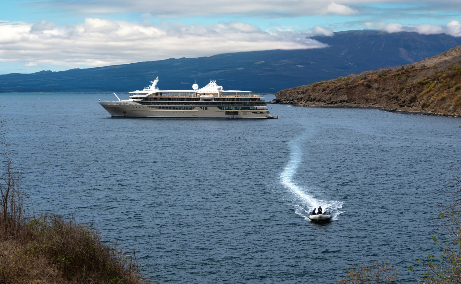 Small luxury expedition ship in the Galápagos with a Zodiac boat traveling between the ship and shore.