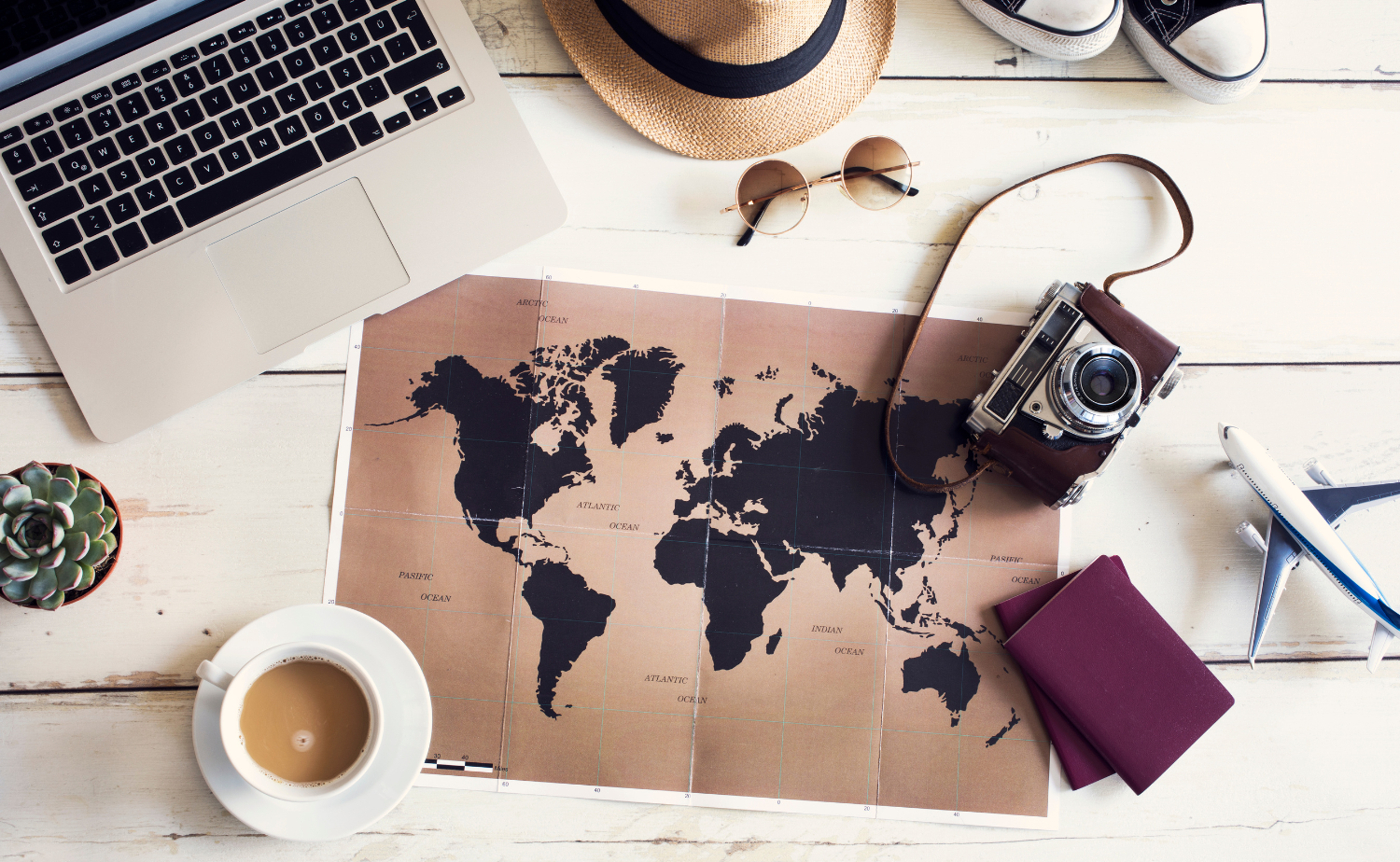 A flat lay featuring a world map, laptop, coffee, camera, passport, and travel accessories arranged for relaxed vacation planning.