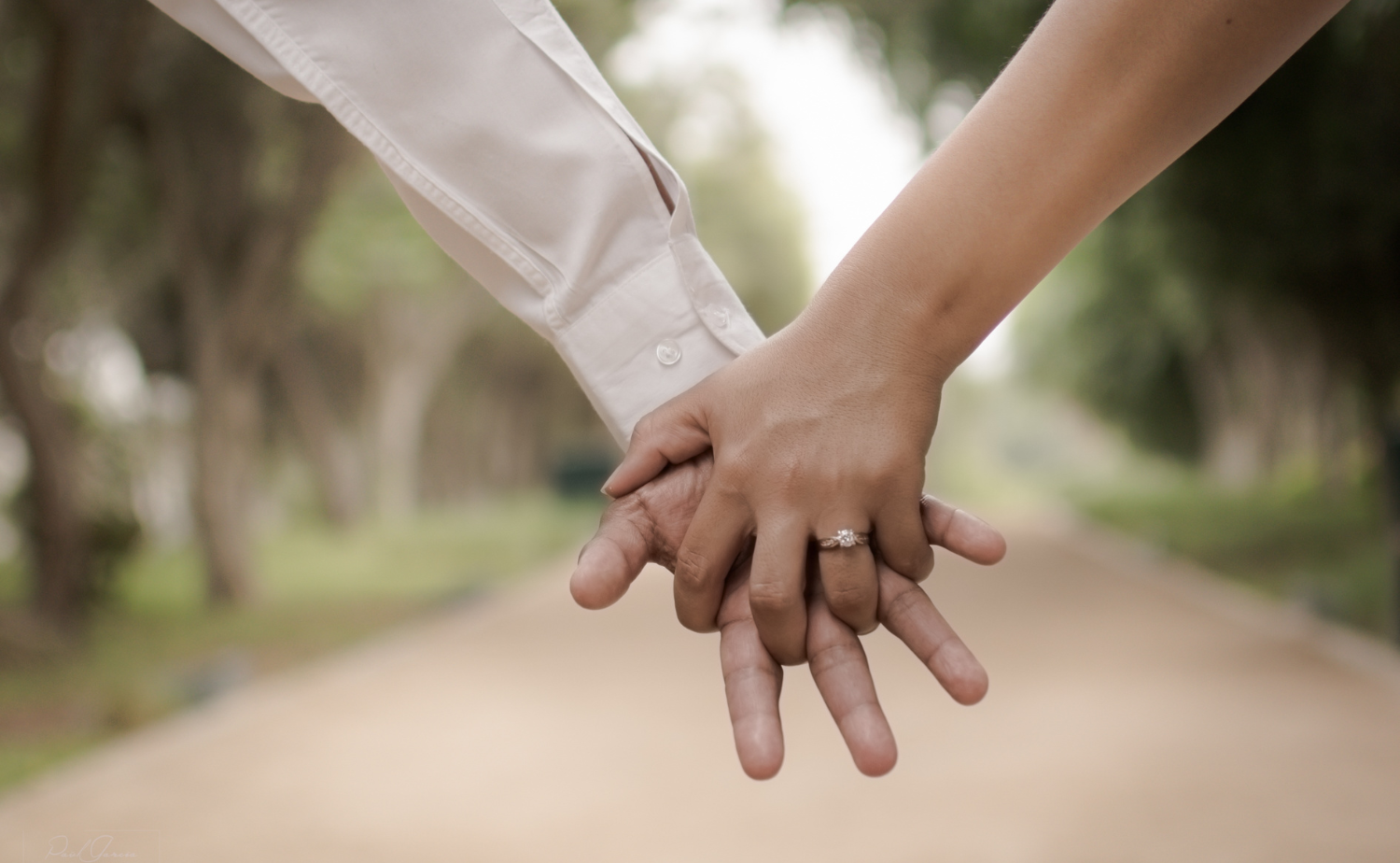 Close-up of a couple holding hands with an engagement ring in focus