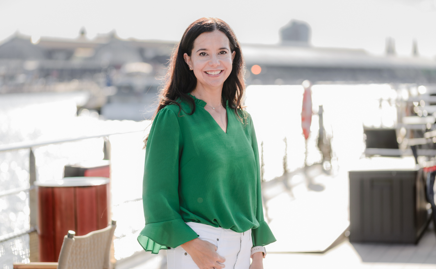 A woman standing on the deck of a river cruise ship with sunlight reflecting on the water behind her.