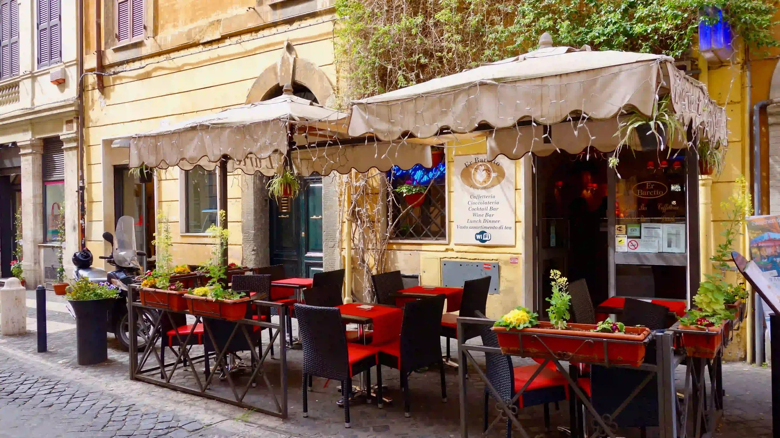 Outdoor café tables with red chairs lining a narrow cobblestone street in Rome.