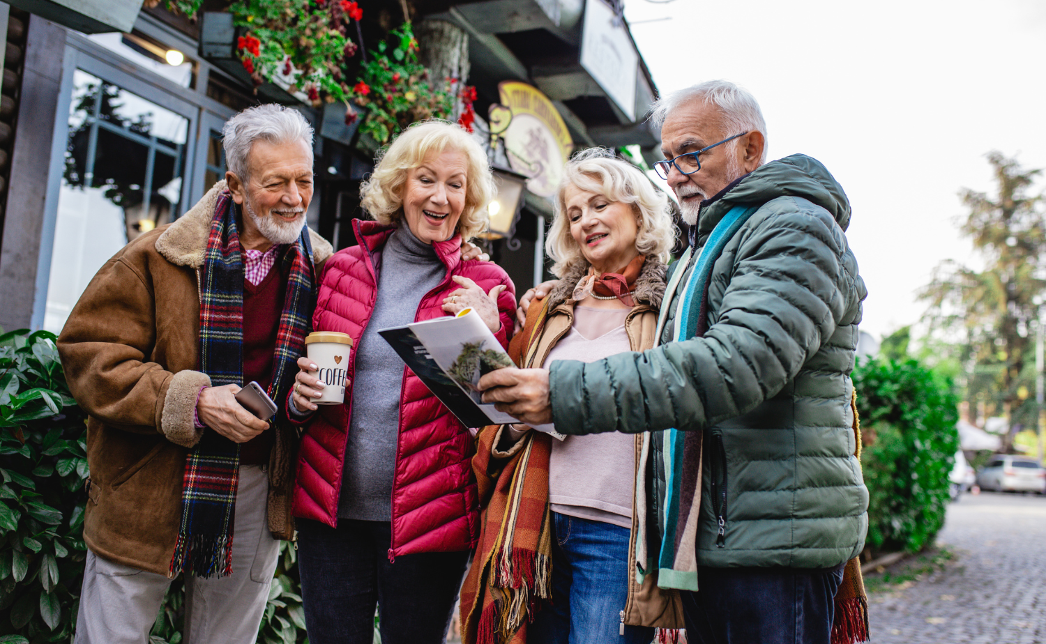 Four smiling travelers dressed for winter look at a map together in a charming European town, highlighting the joy of shared experiences while traveling during the holidays