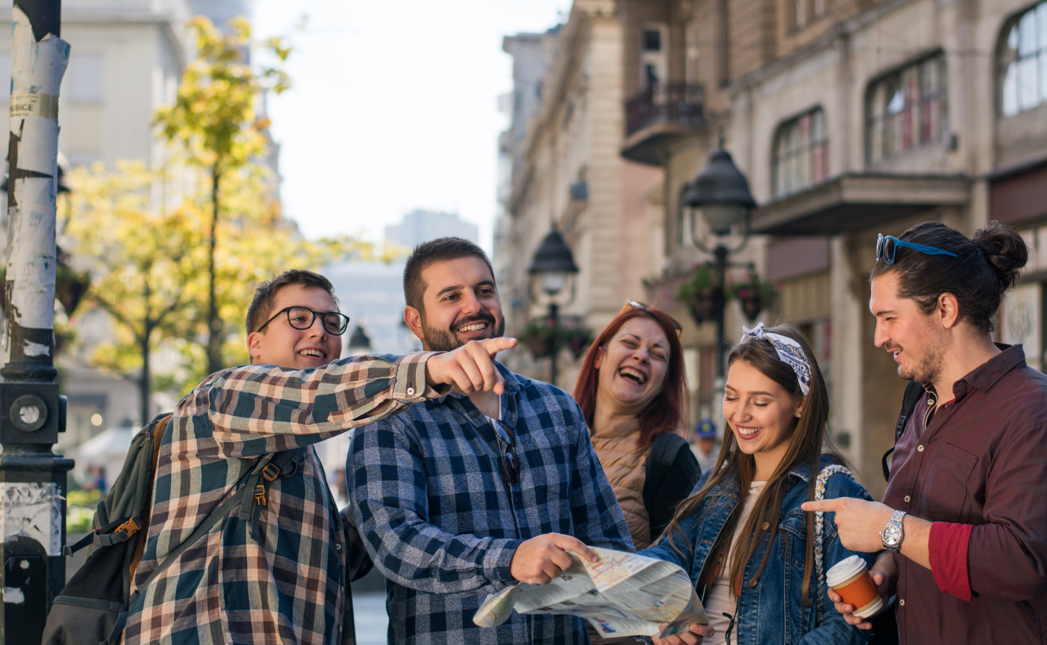 Group of friends laughing and reviewing a city map while exploring a European destination together.