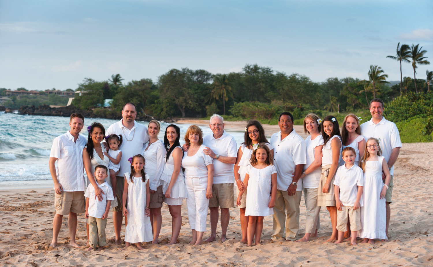 A large multi-generational family dressed in white on a Hawaiian beach at sunset.