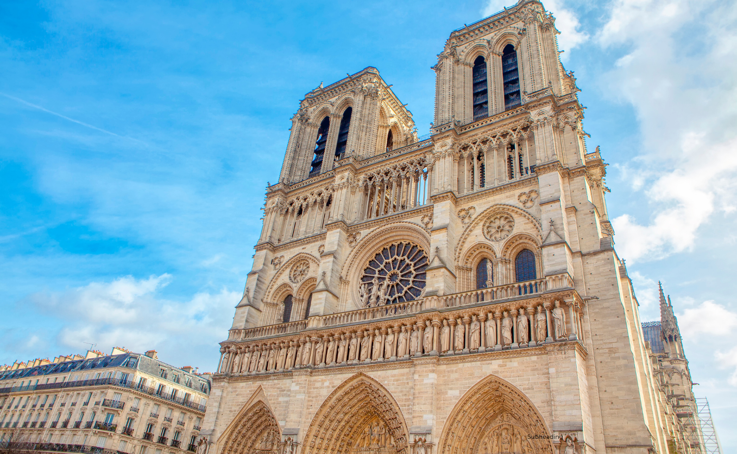 The famous Notre Dame Cathedral in Paris with its two towers and ornate Gothic façade against a bright blue sky.