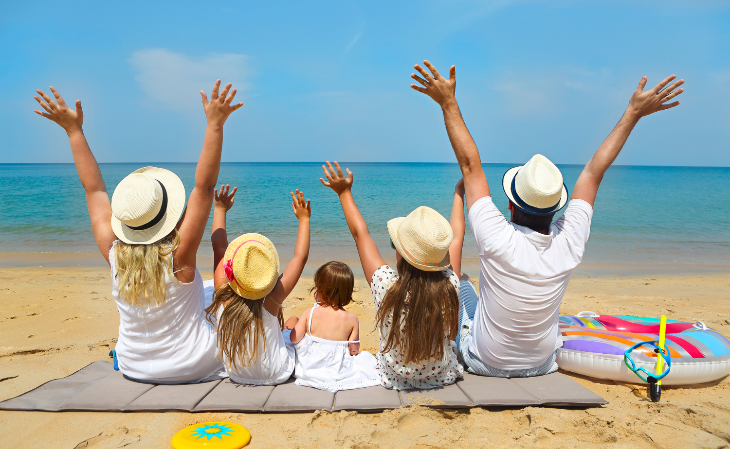A family sitting together on a sandy Caribbean beach with arms raised toward the ocean.