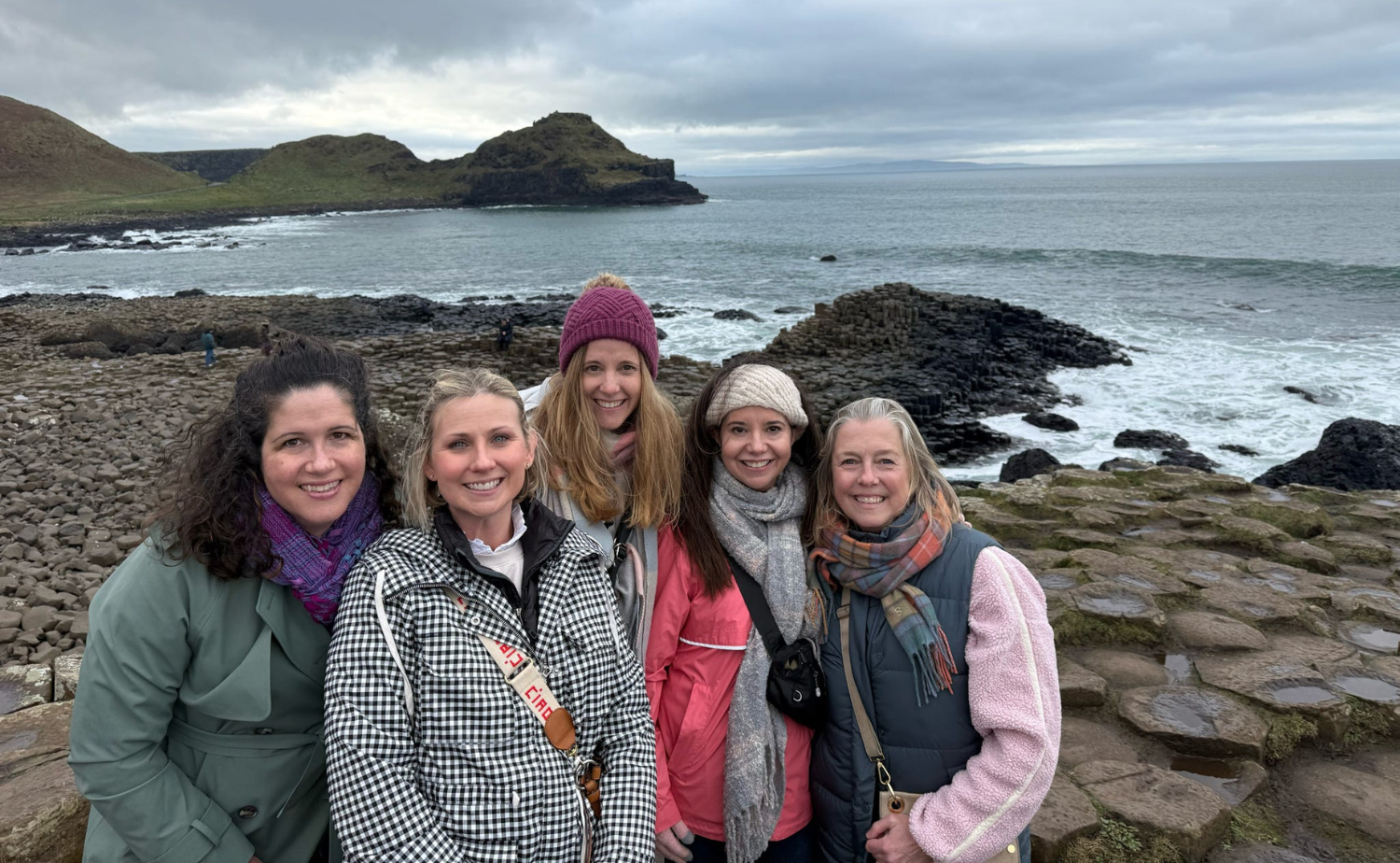 Five women standing together at Giant’s Causeway in Northern Ireland with the basalt columns and dramatic coastline visible behind them.
