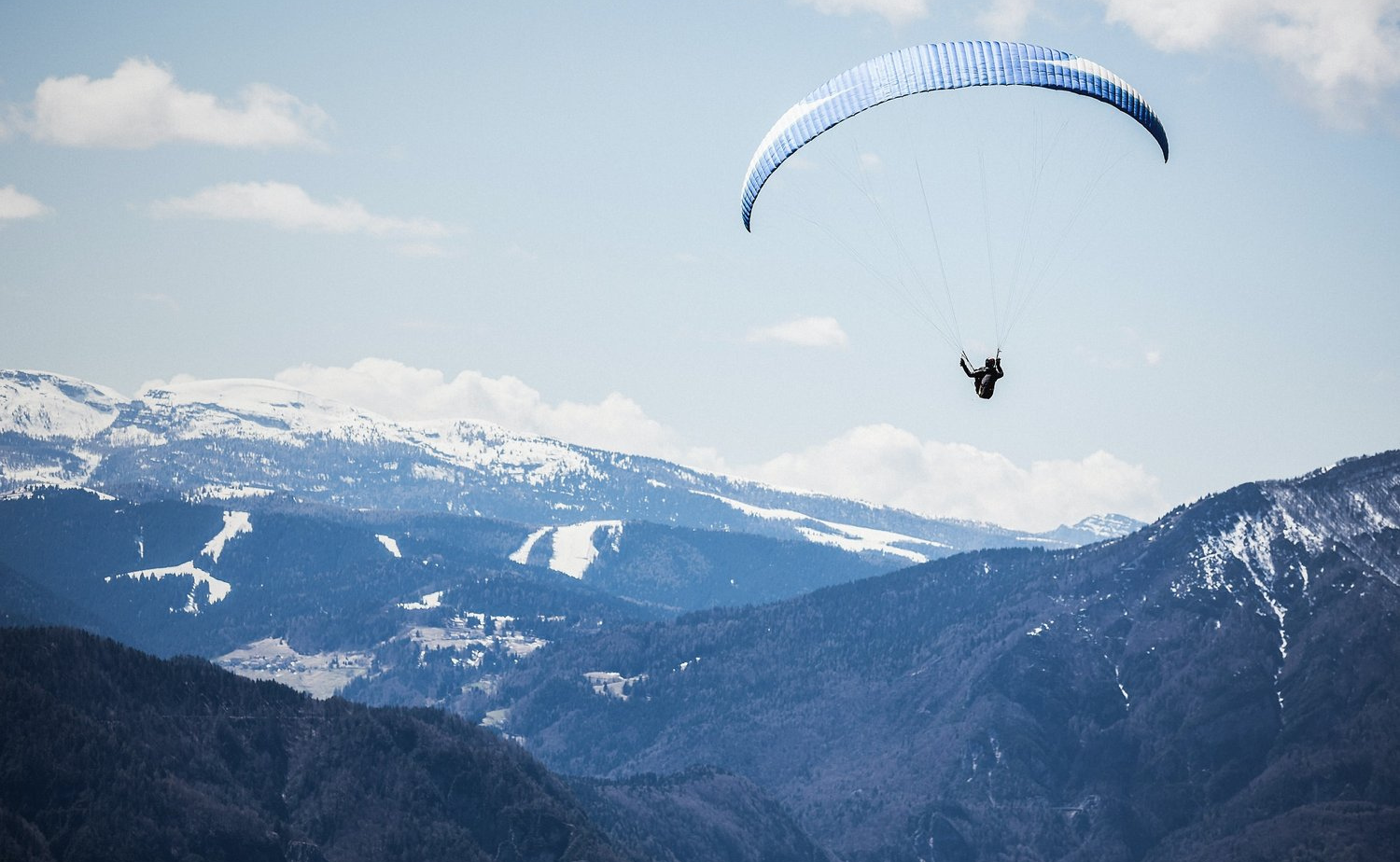 A paraglider floats high above snow-covered Alaskan mountains.