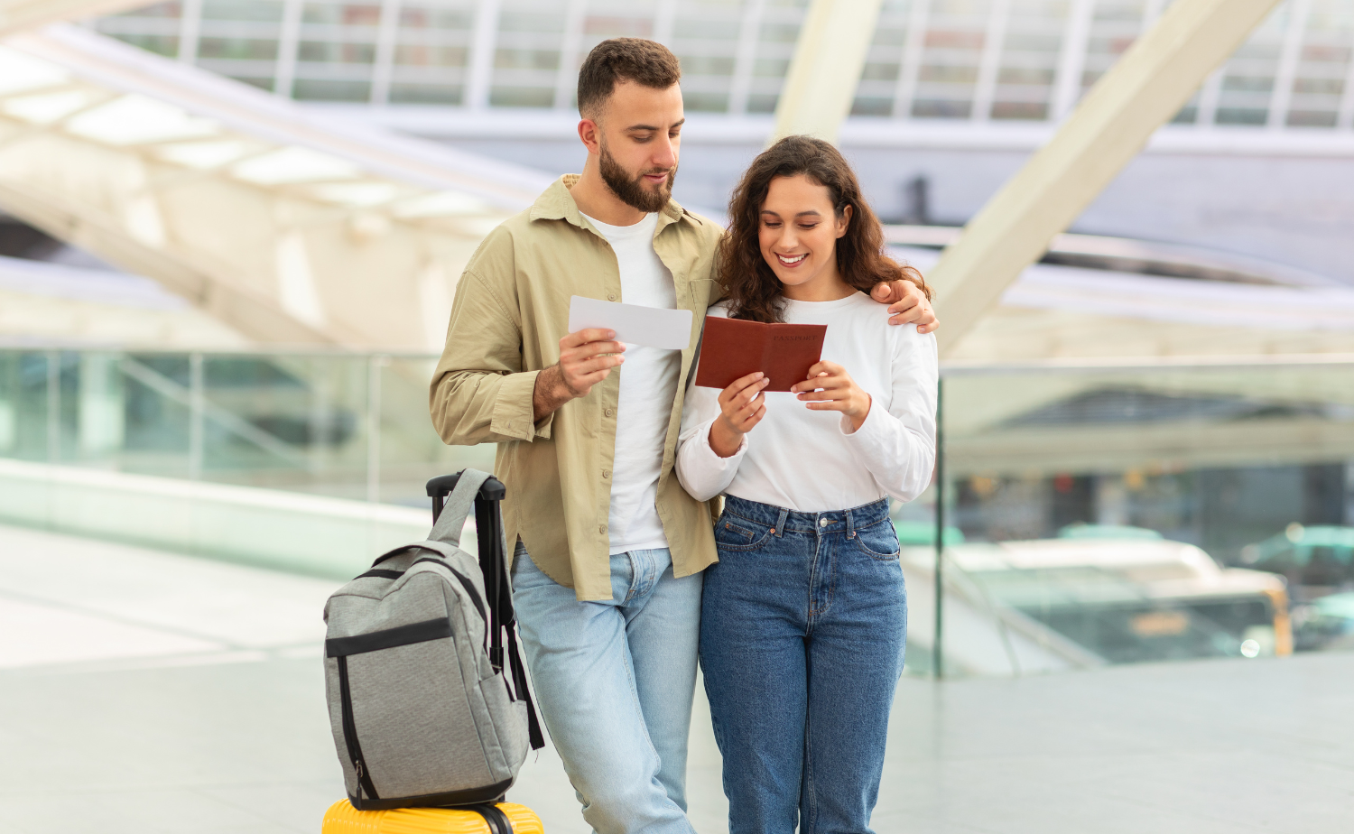A couple at the airport reviewing travel documents and a passport while standing beside luggage.
