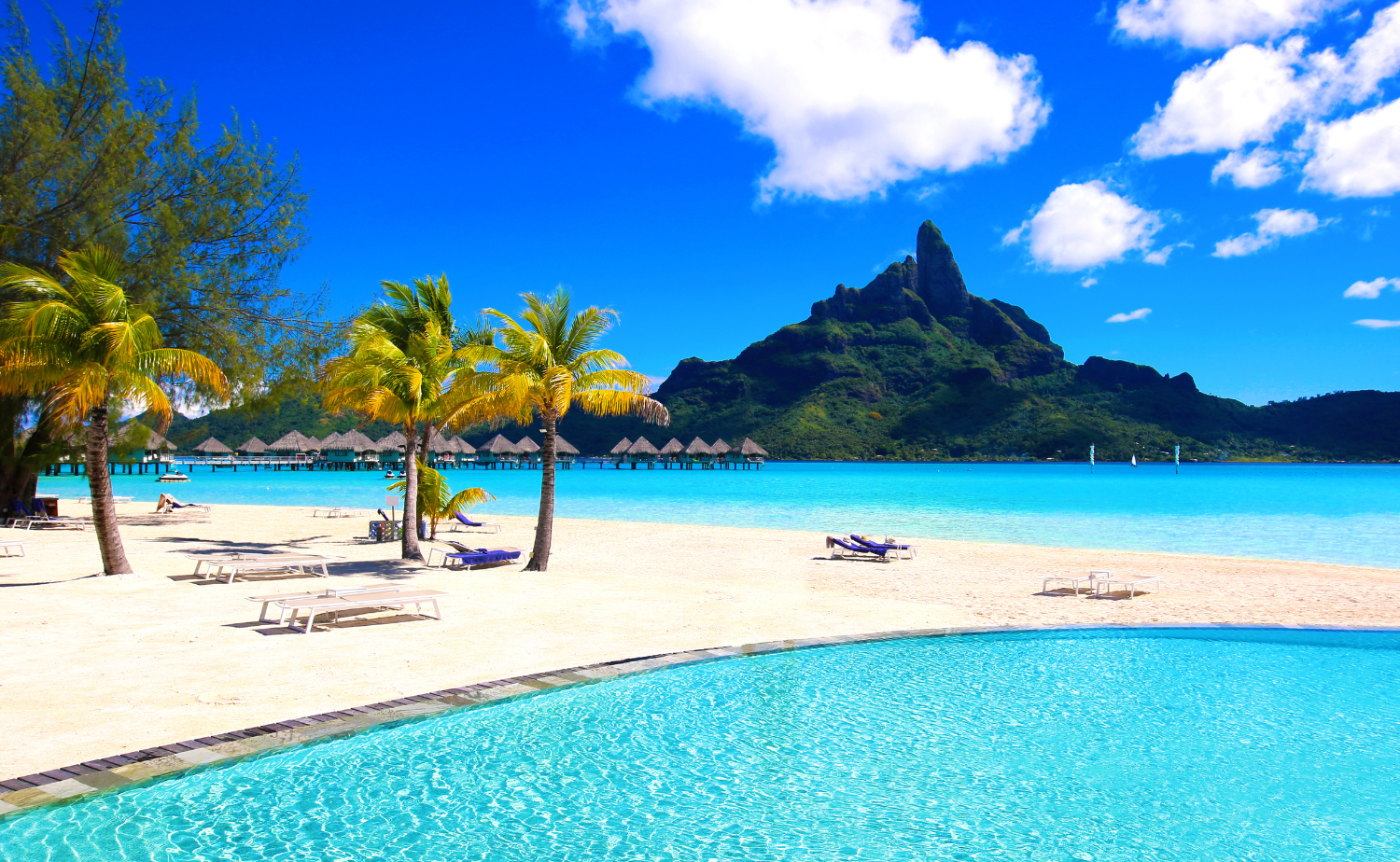 Bora Bora beach with turquoise lagoon, overwater bungalows and a dramatic green mountain in French Polynesia.