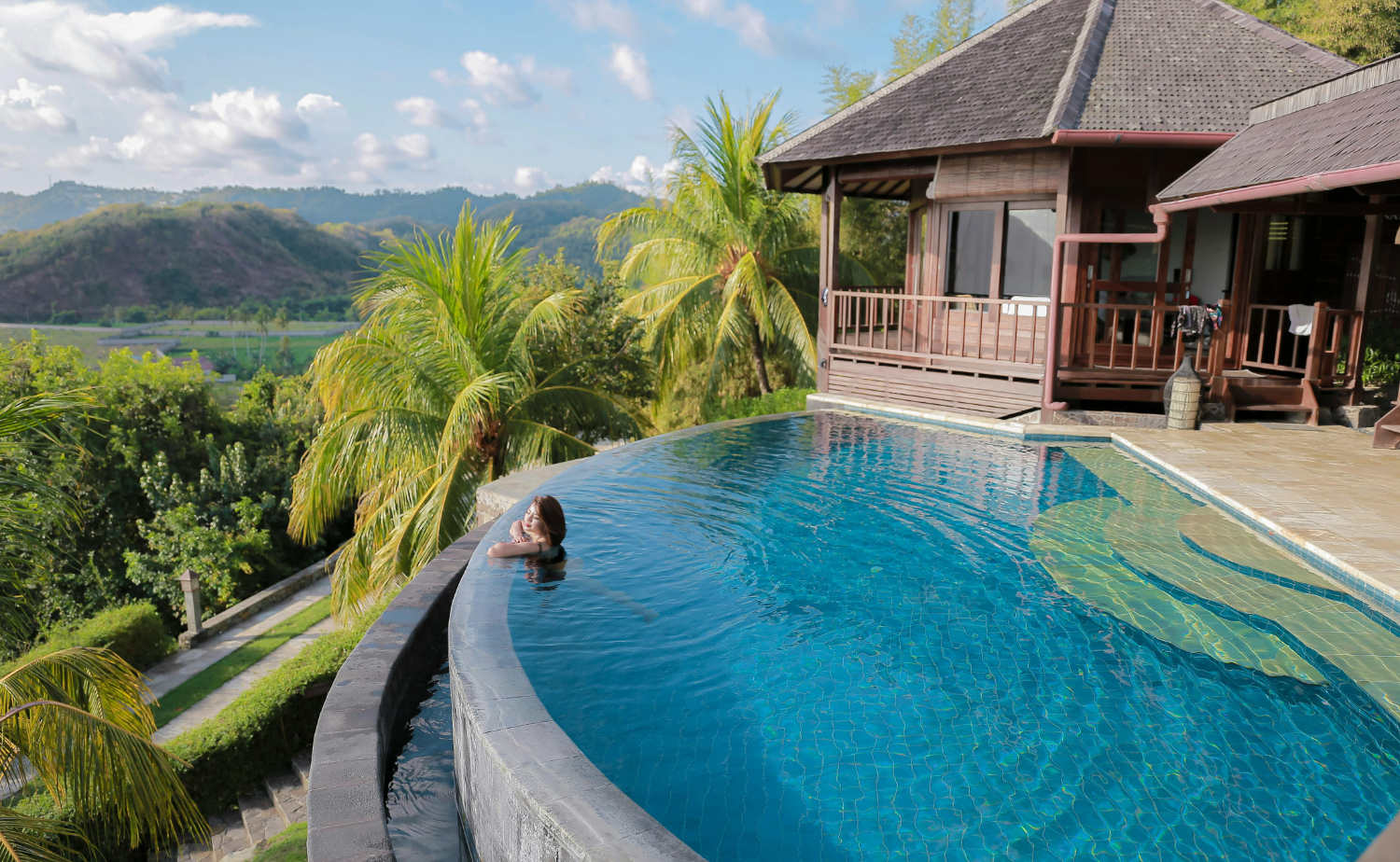 A woman enjoying an infinity pool overlooking a lush tropical landscape at a luxury villa.