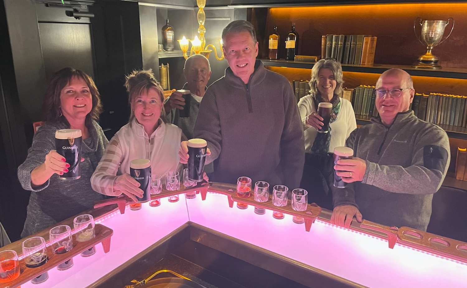 Group of travelers raising pints of Guinness during a tasting experience inside a Dublin brewery setting.