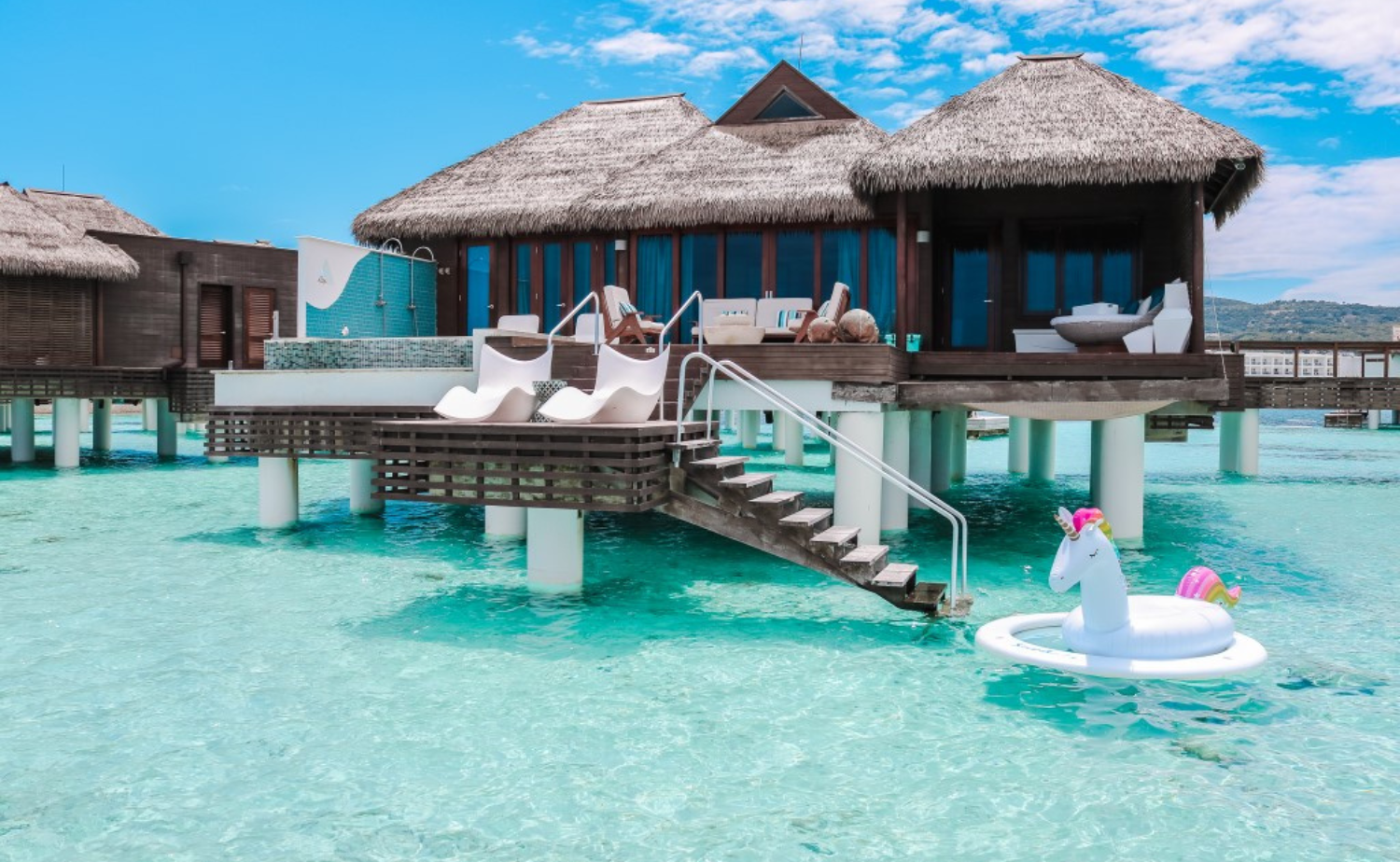 An overwater bungalow villa with a private deck and steps leading directly into a clear turquoise lagoon.