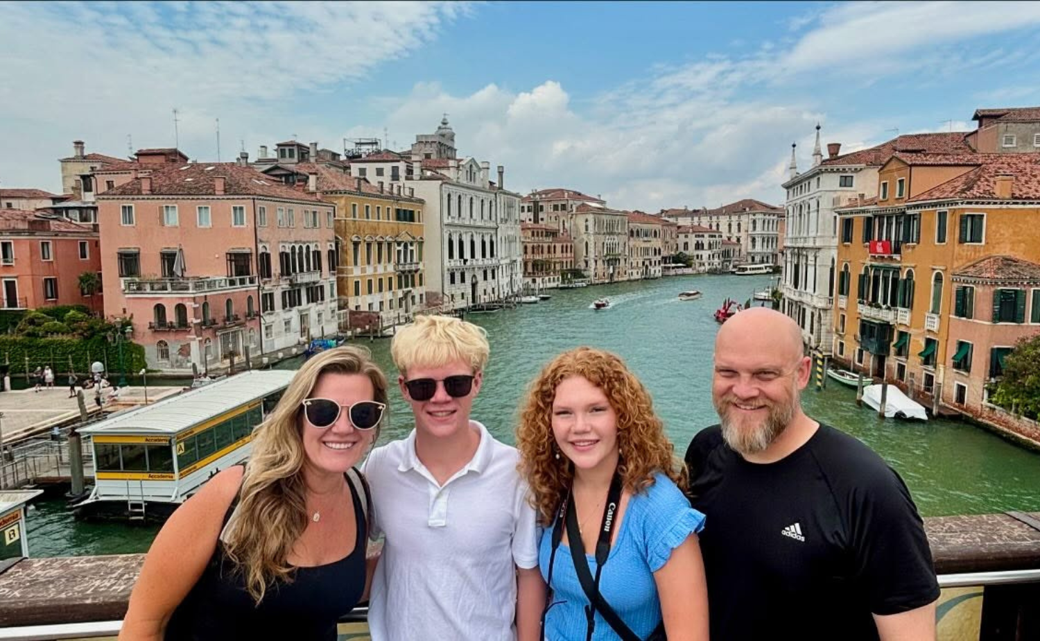 A family of four smiling together along the Grand Canal in Venice during a graduation celebration trip through Italy.