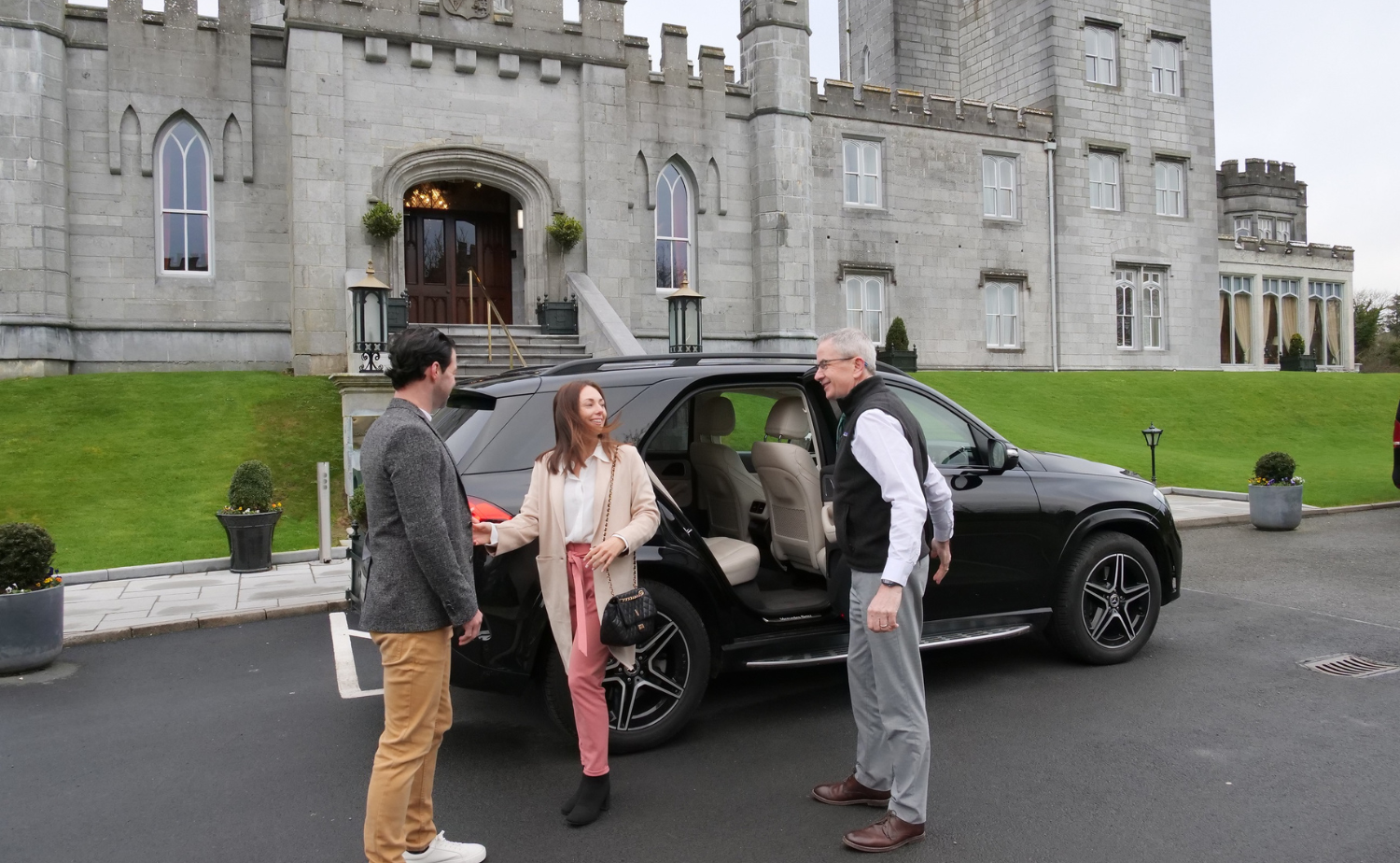 A couple stepping out of a private vehicle in front of a historic Irish castle with a driver assisting them.