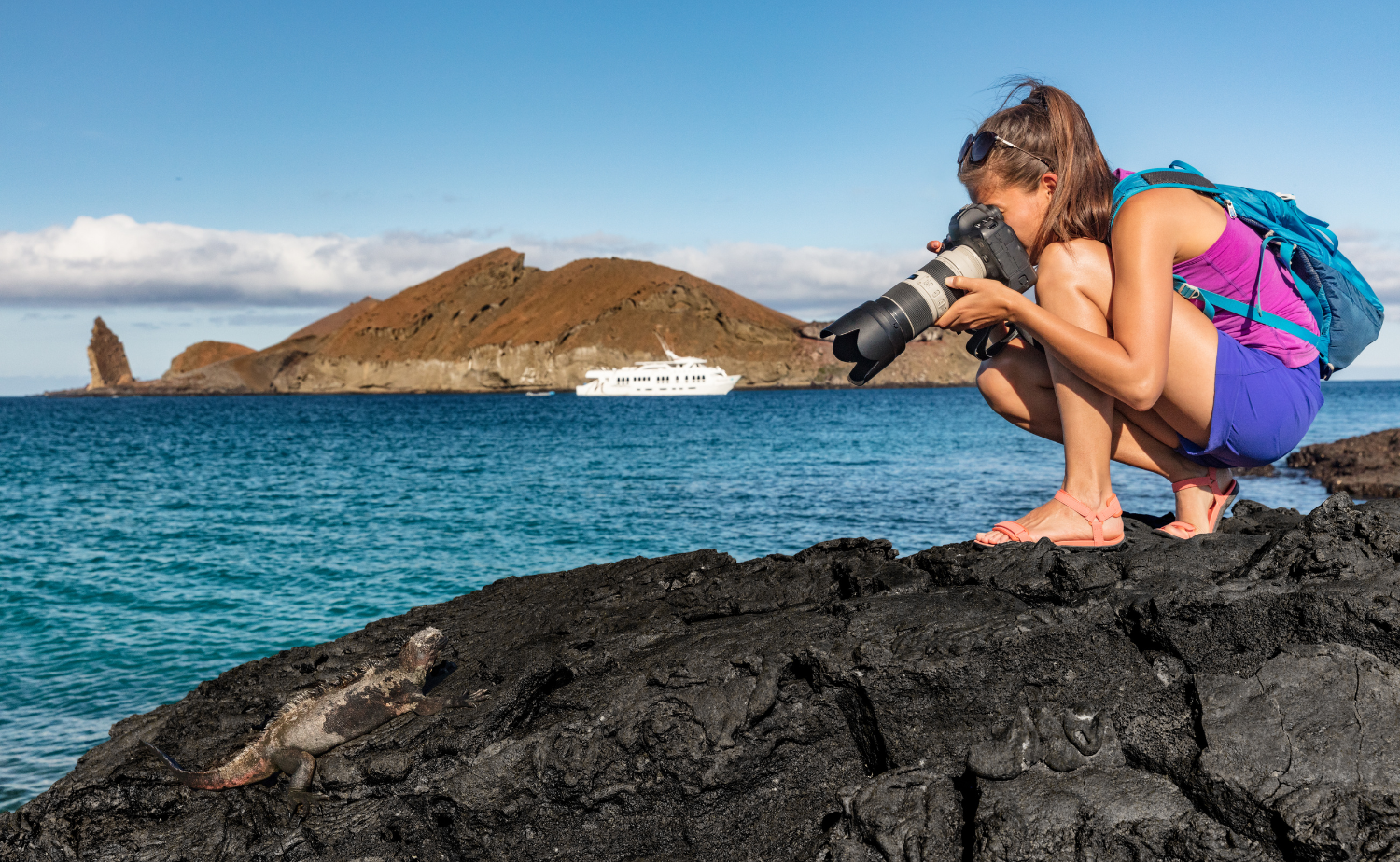 Traveler photographing a marine iguana on volcanic rocks during a Galápagos expedition.