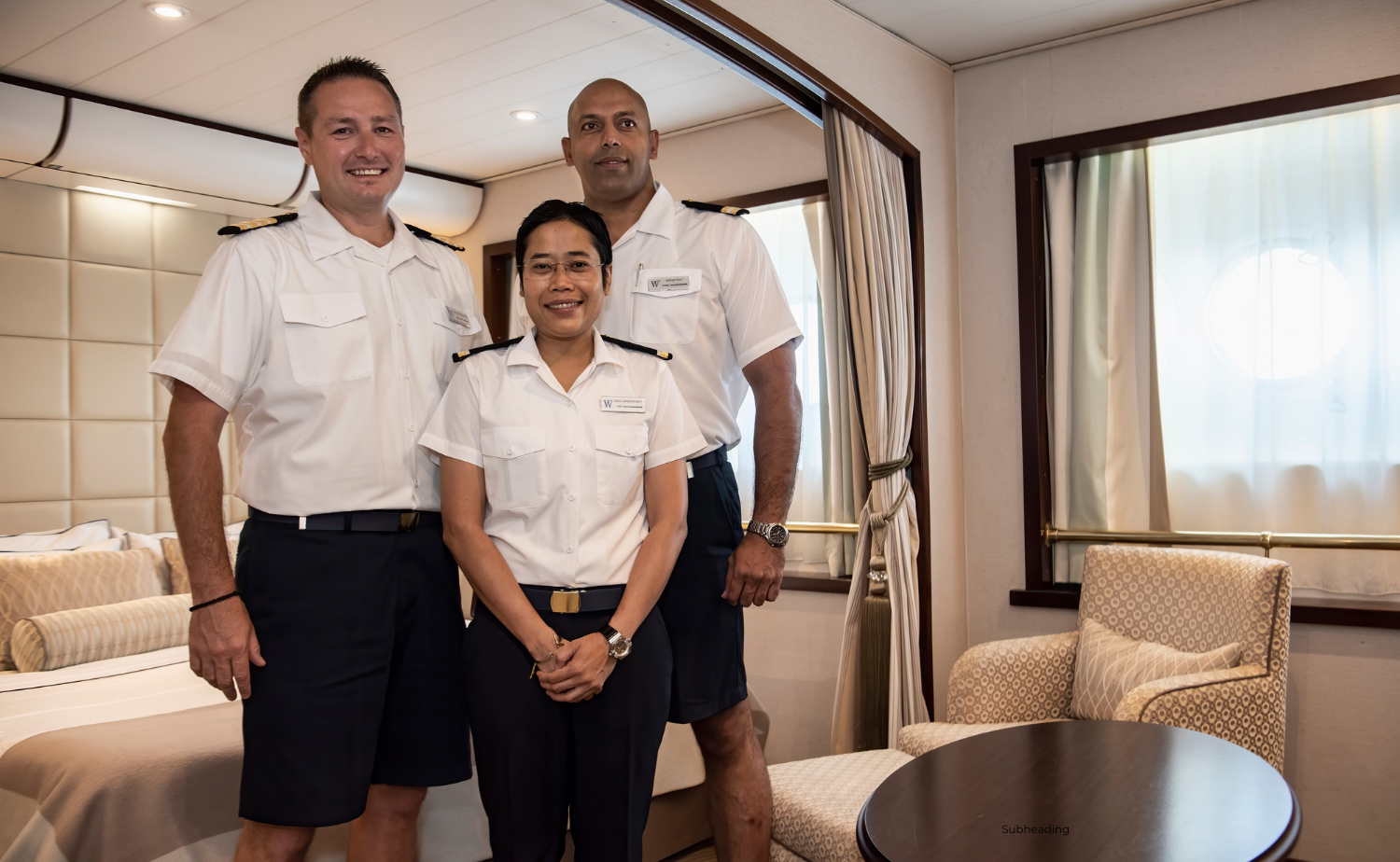 Three Windstar crew members smiling and posing inside a well-appointed suite on board.