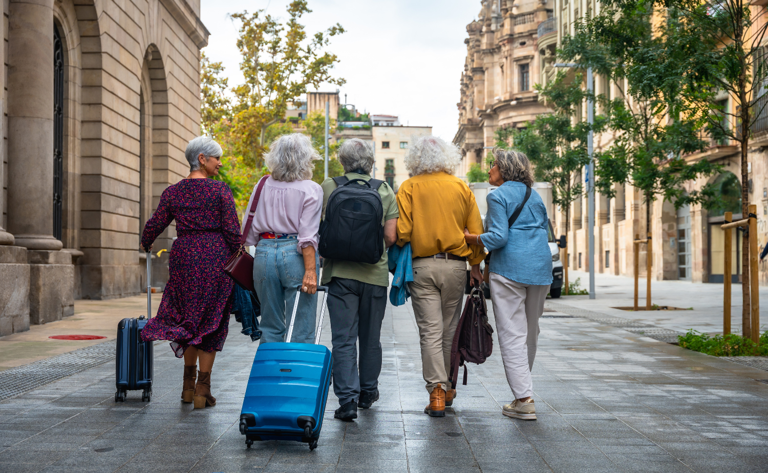 Group of mature travelers walking through a European city with luggage and backpacks.