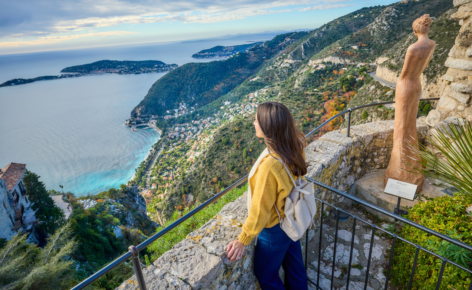 A woman in a yellow sweater admires the sweeping coastal views from Èze, France.