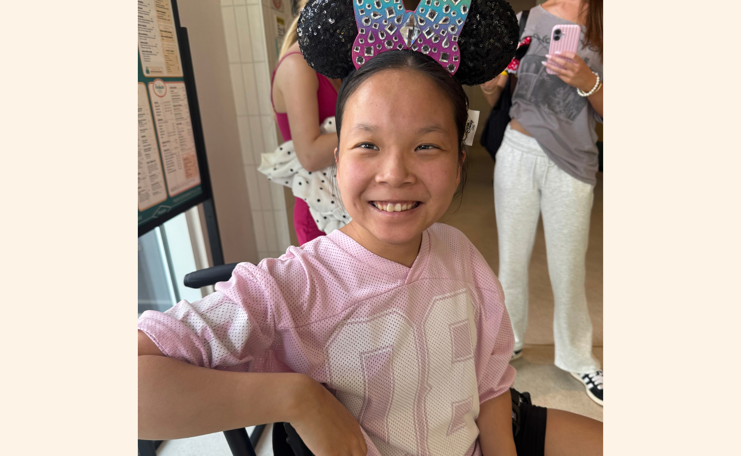 Hannah smiling in her wheelchair and wearing sparkly Minnie Mouse ears during her Disneyland vacation.