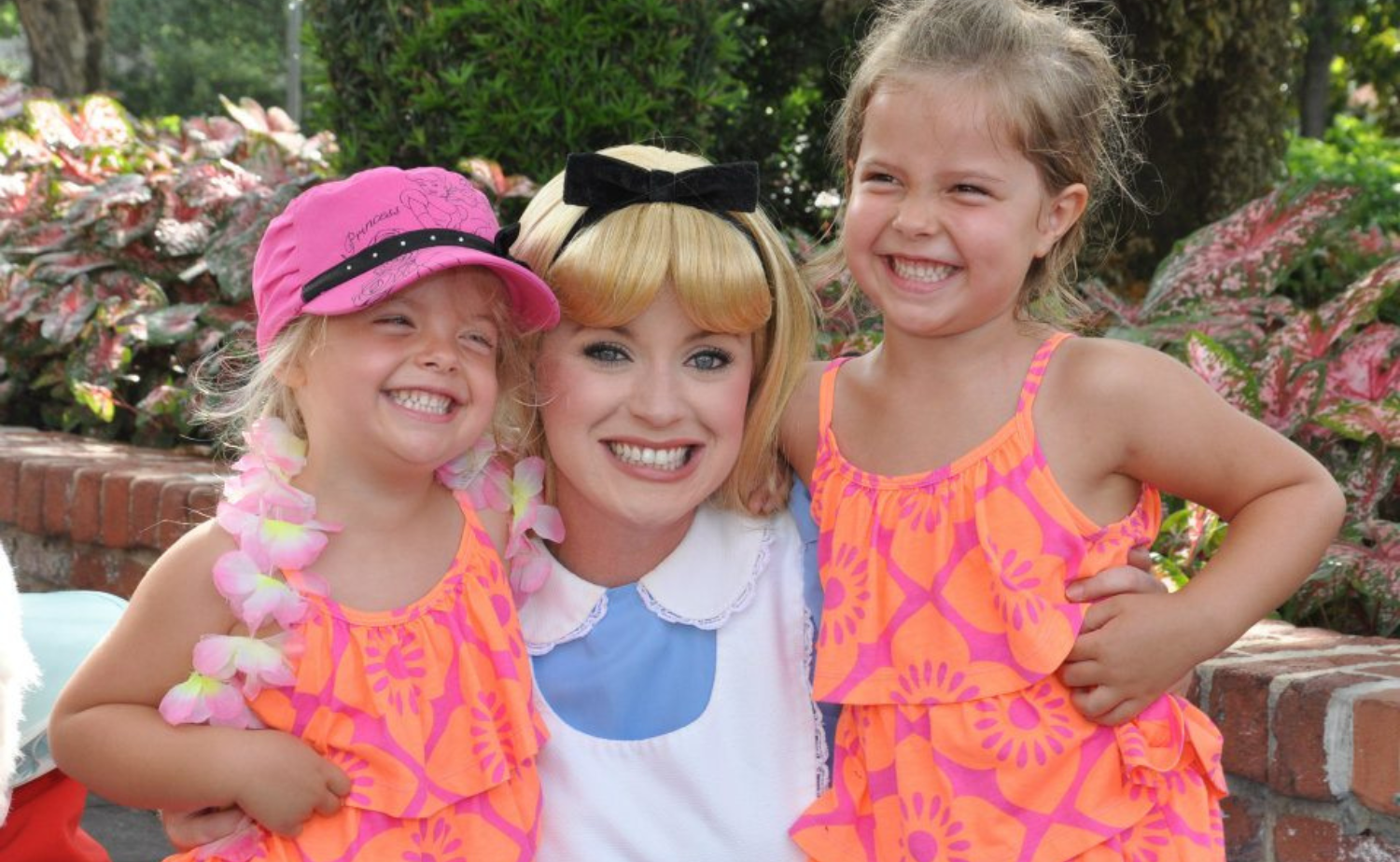 Two young girls smiling with a costumed character during a joyful childhood vacation experience.