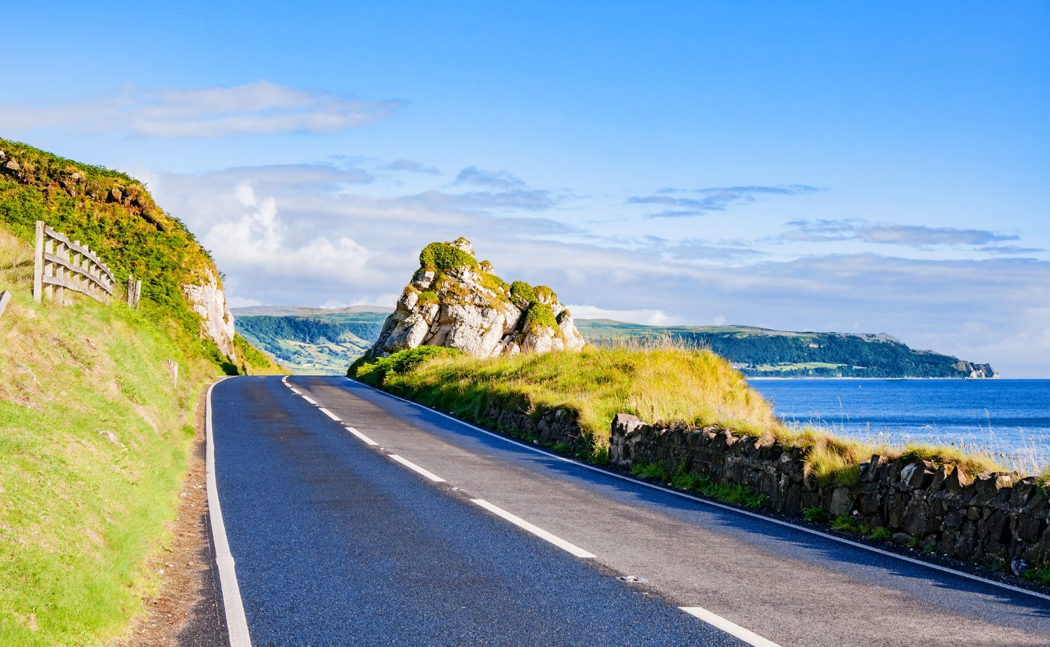 A scenic coastal road along the Antrim Coast with cliffs, green hills, and ocean views.