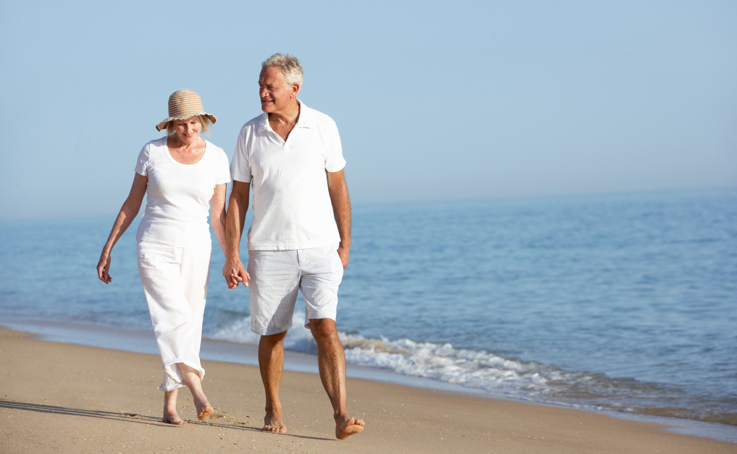 A retired couple walking hand in hand along a quiet beach during a relaxing seaside vacation.