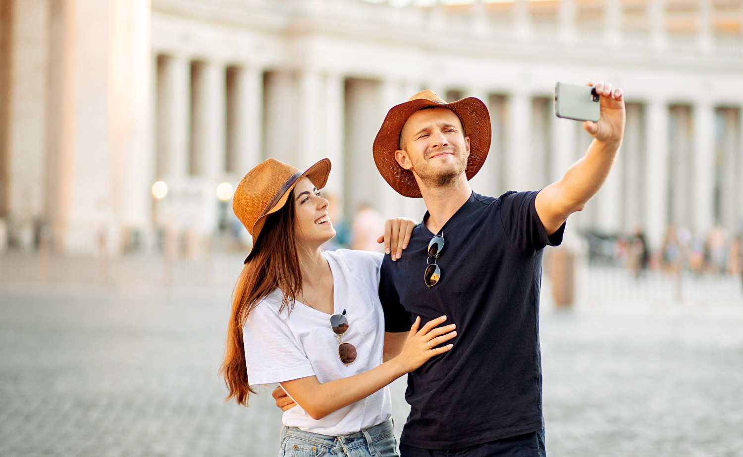 A smiling couple takes a selfie together in a historic European square.