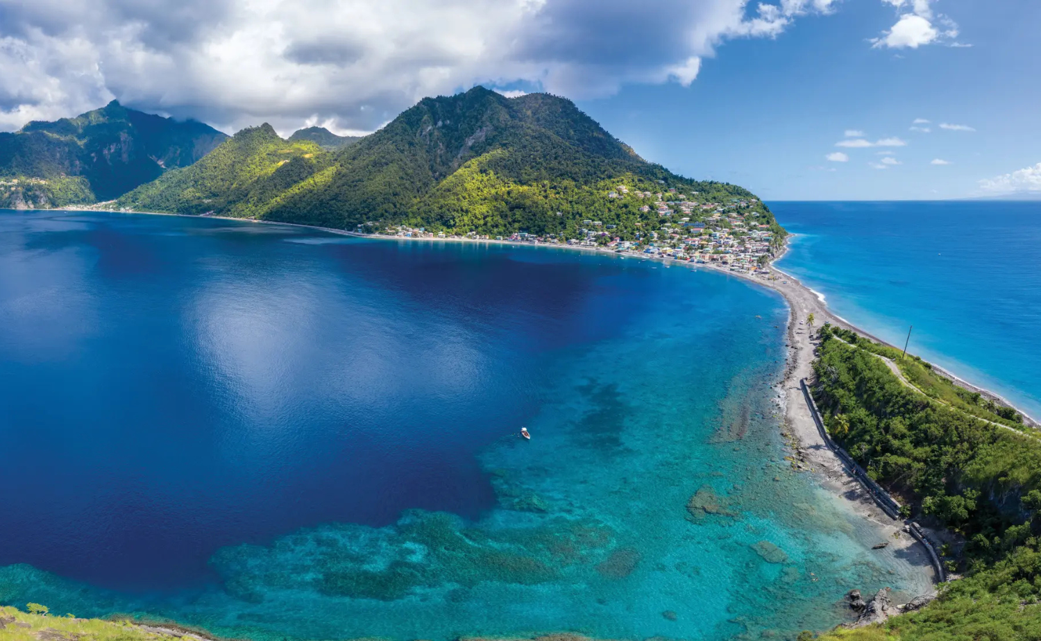 Aerial view of Dominica's lush mountains, dramatic coastline, and clear blue Caribbean water.