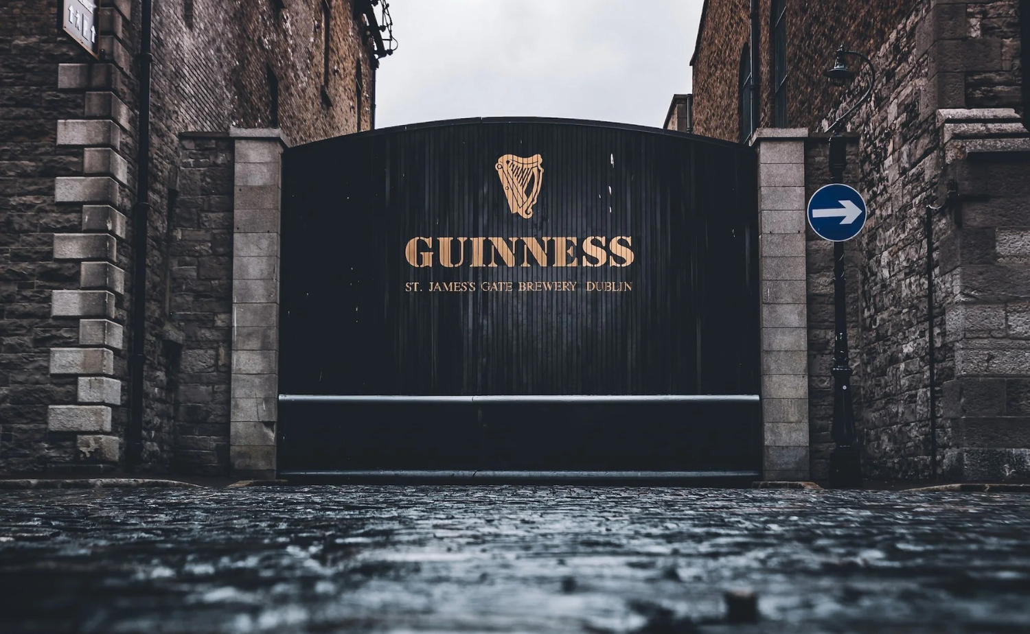 The entrance gate of the Guinness Storehouse in Dublin on a wet cobblestone street.
