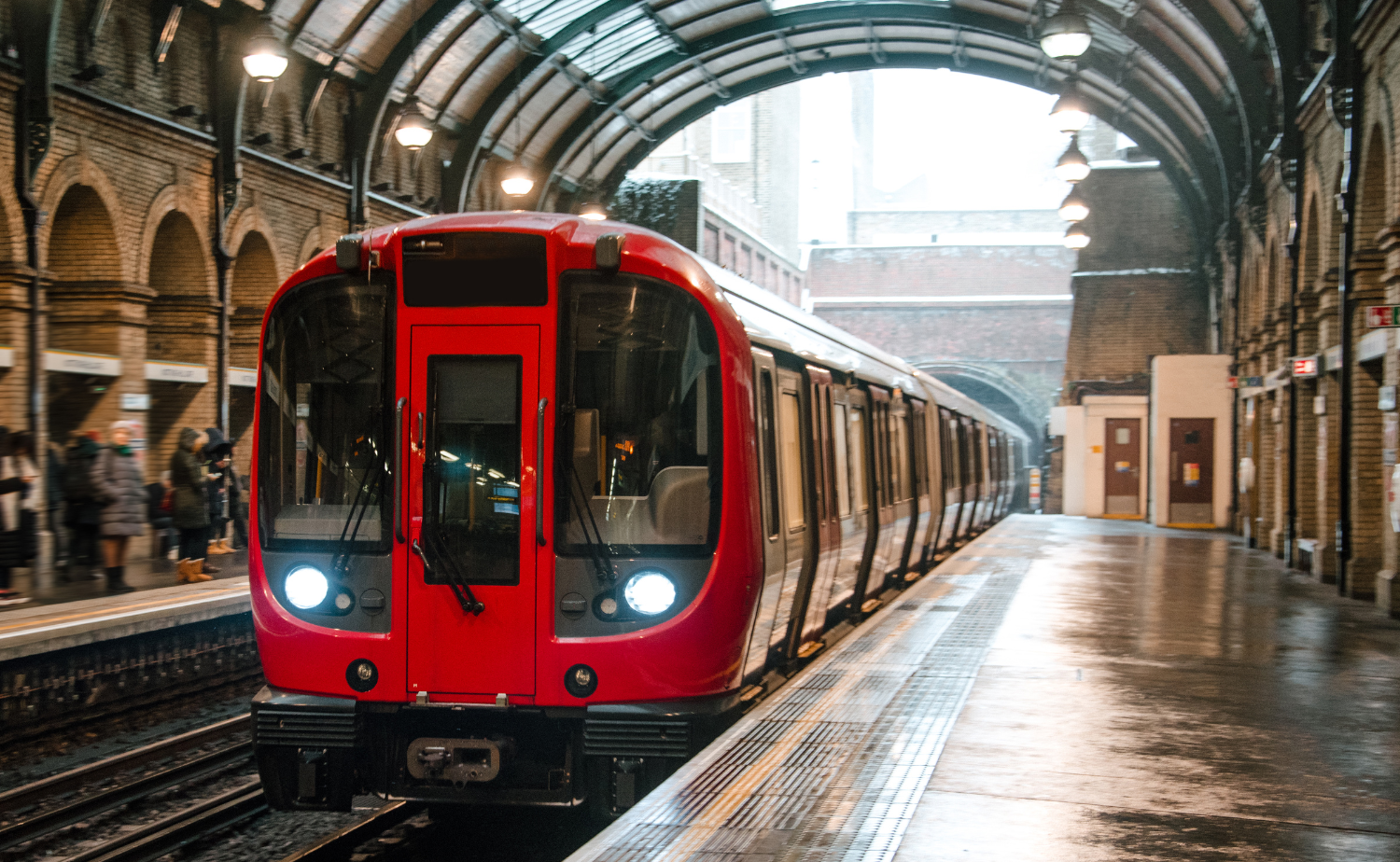 Red train stopped at a covered London train platform inside a historic arched station.
