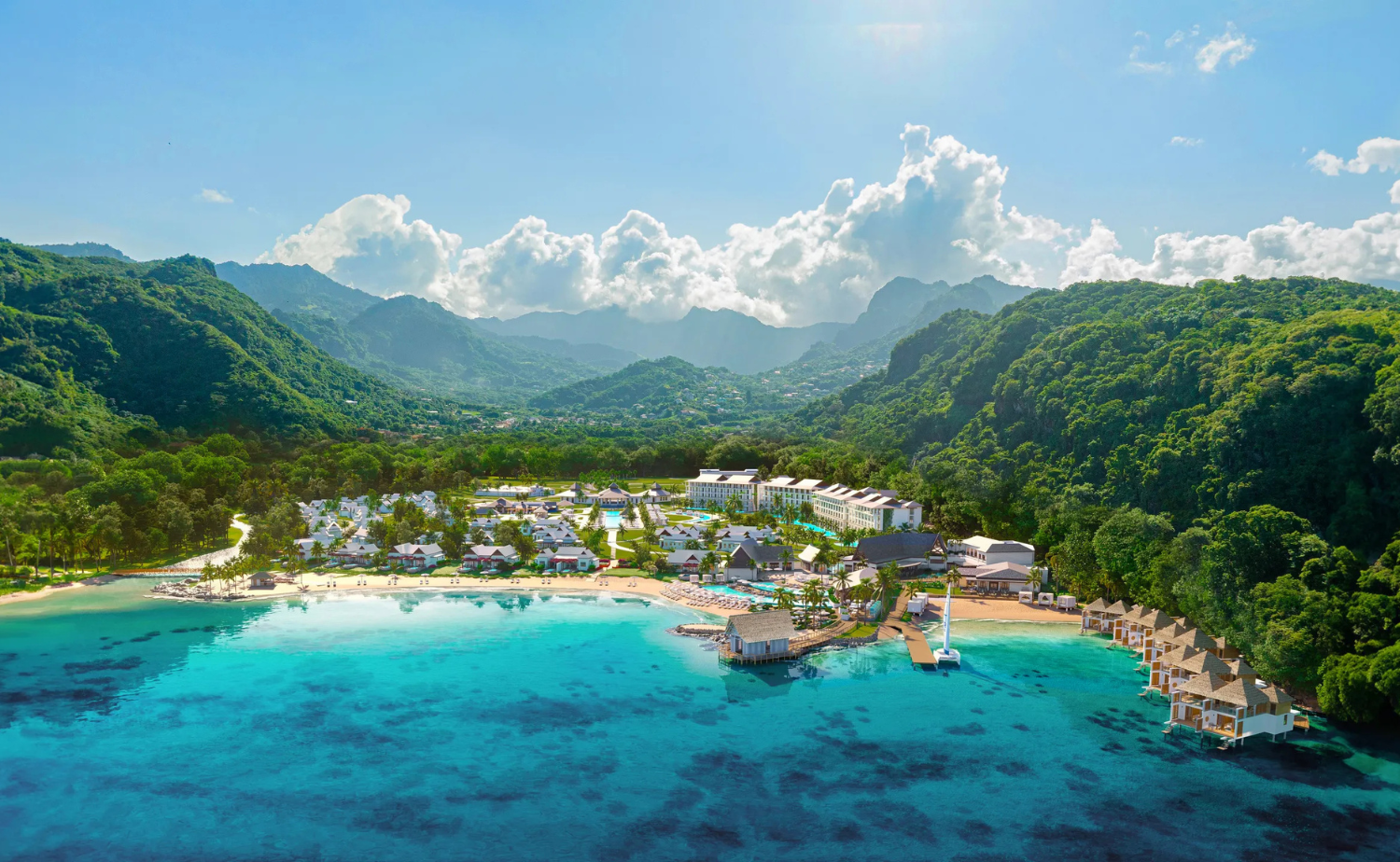 Overwater villas and beachfront accommodations at Sandals St. Vincent surrounded by lush mountains and clear blue water.
