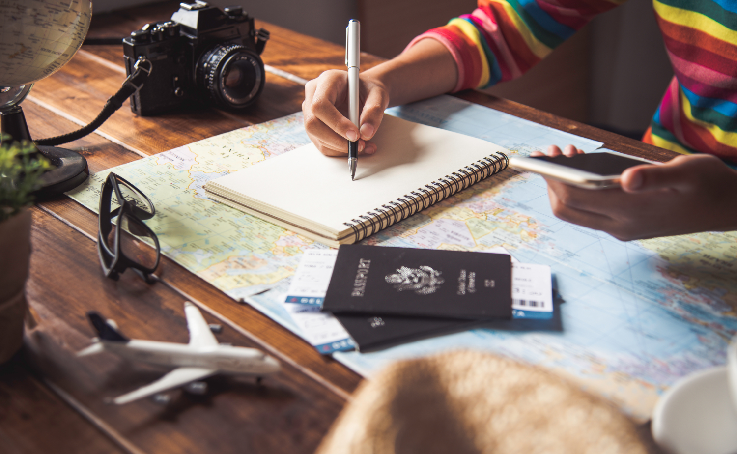 A traveler planning a trip with a notebook, passport, phone, and map laid out on a wooden desk.