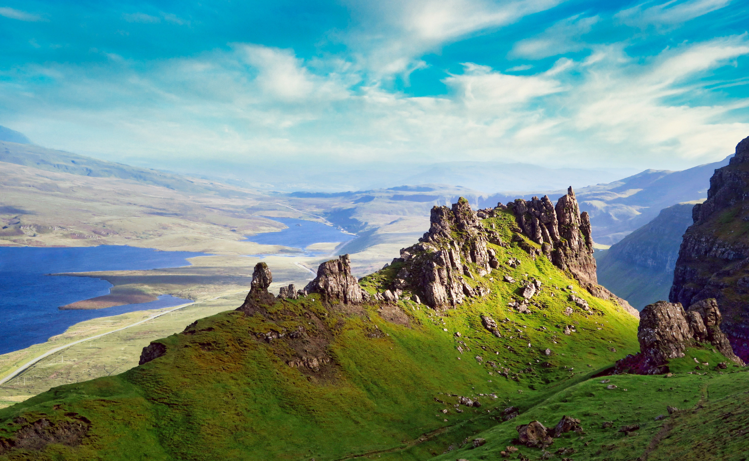 A sweeping panoramic view of the Scottish Highlands with rugged cliffs, green hills, and misty atmosphere.