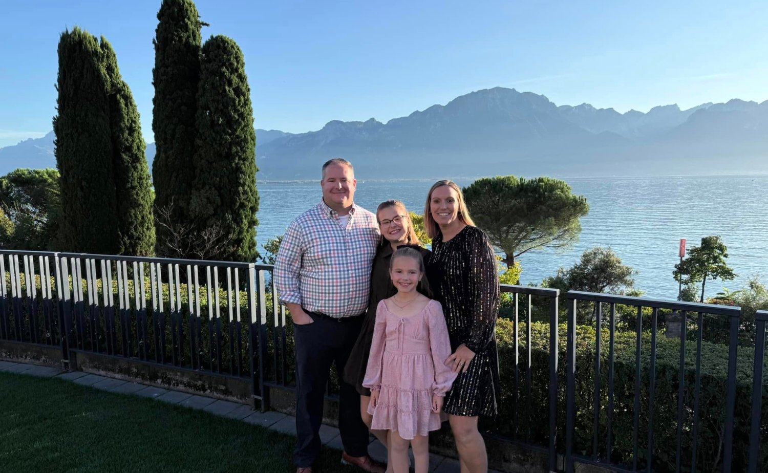 A family posing in front of a lake and mountains in Switzerland on a sunny day.
