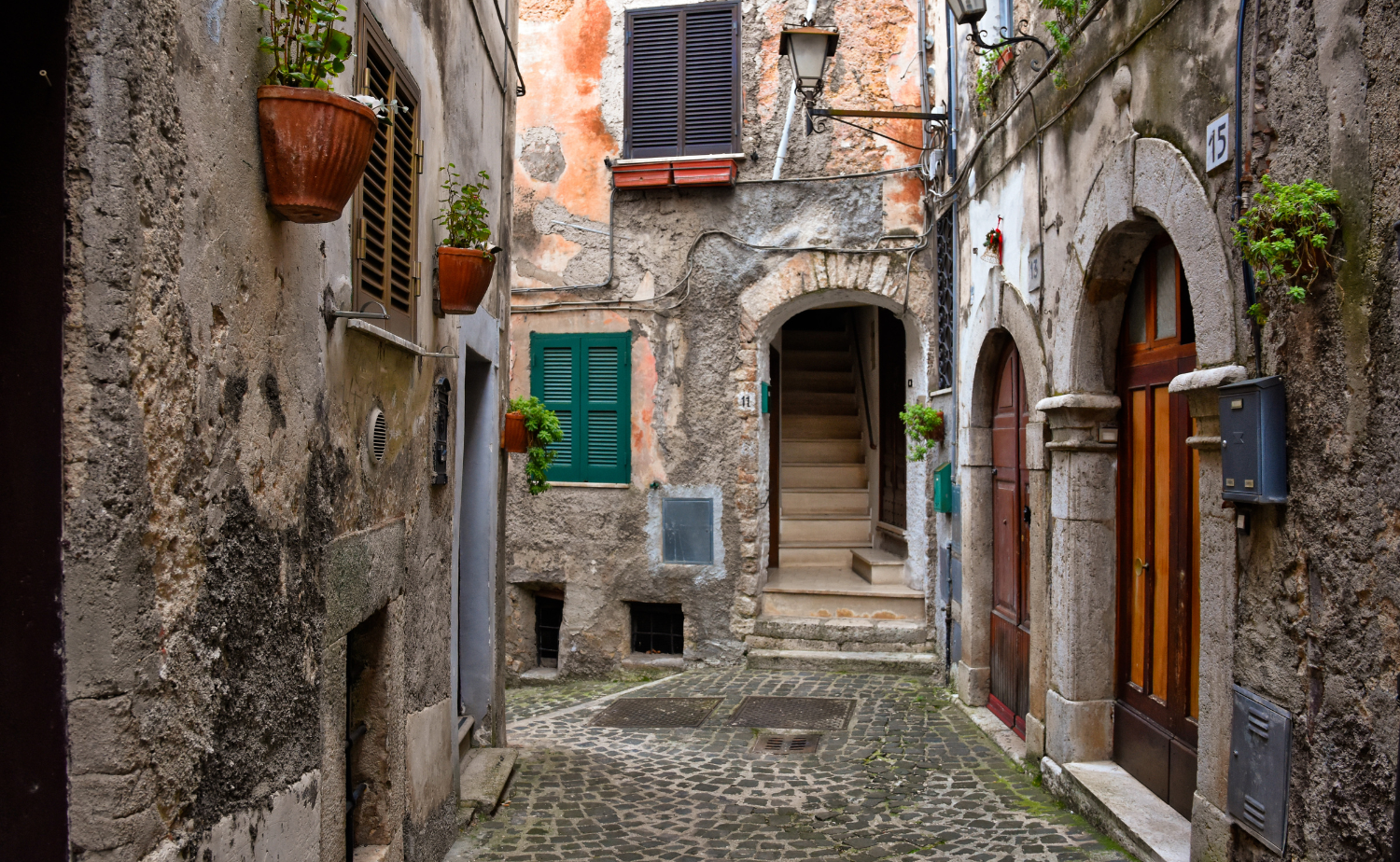 Narrow stone alleyway with historic homes and flower pots in the charming hill town of Guarcino in Italy's Lazio region.