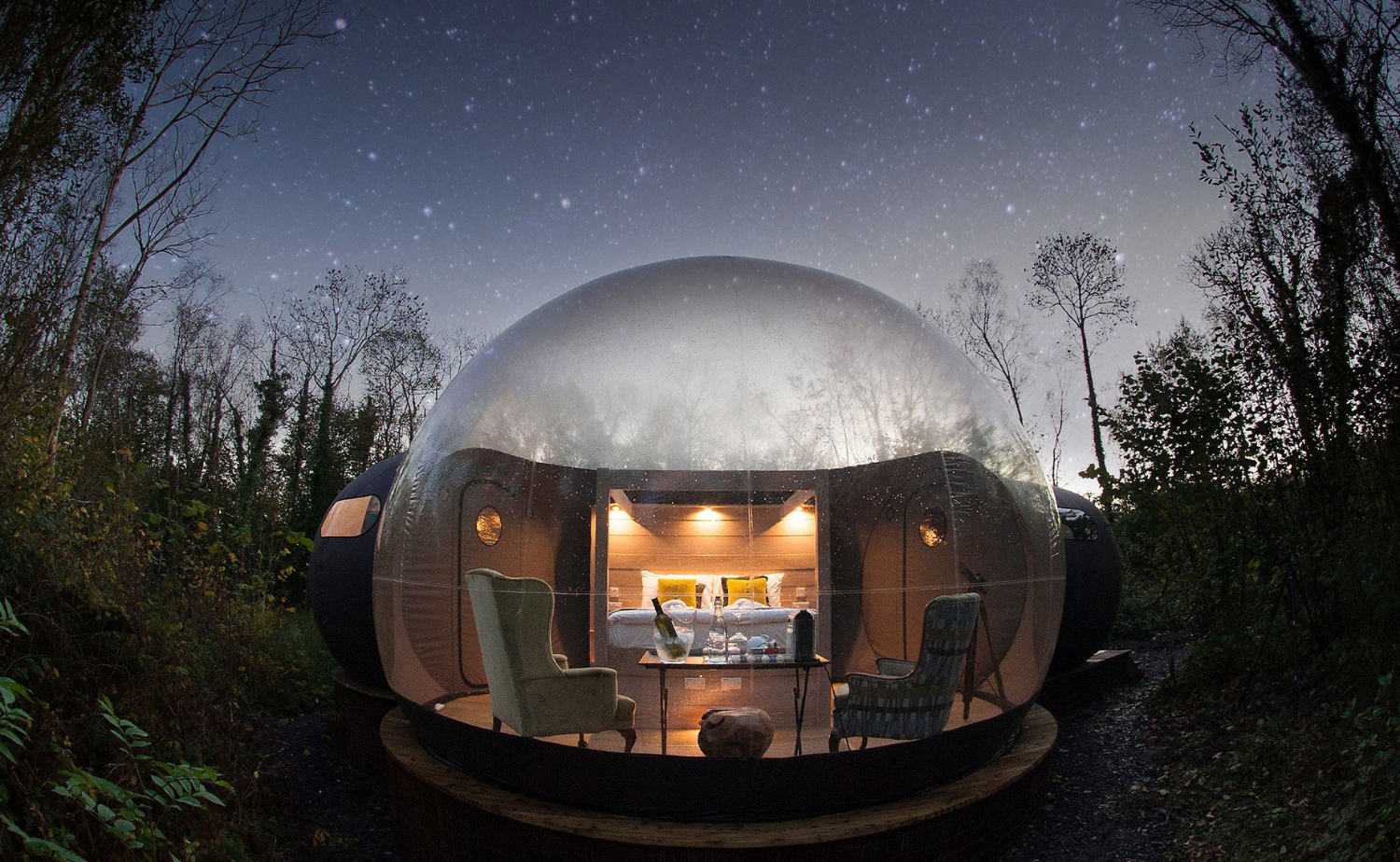 Exterior of a bubble dome at Finn Lough glowing beneath a star-filled night sky, surrounded by trees in Northern Ireland.